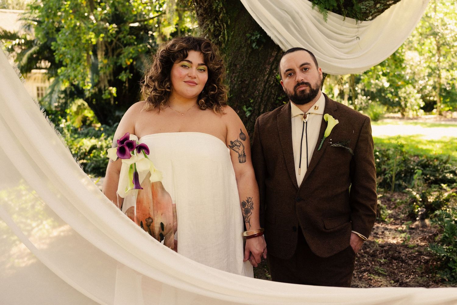 A wedding ceremony takes place in a garden setting with white draping and natural decor.