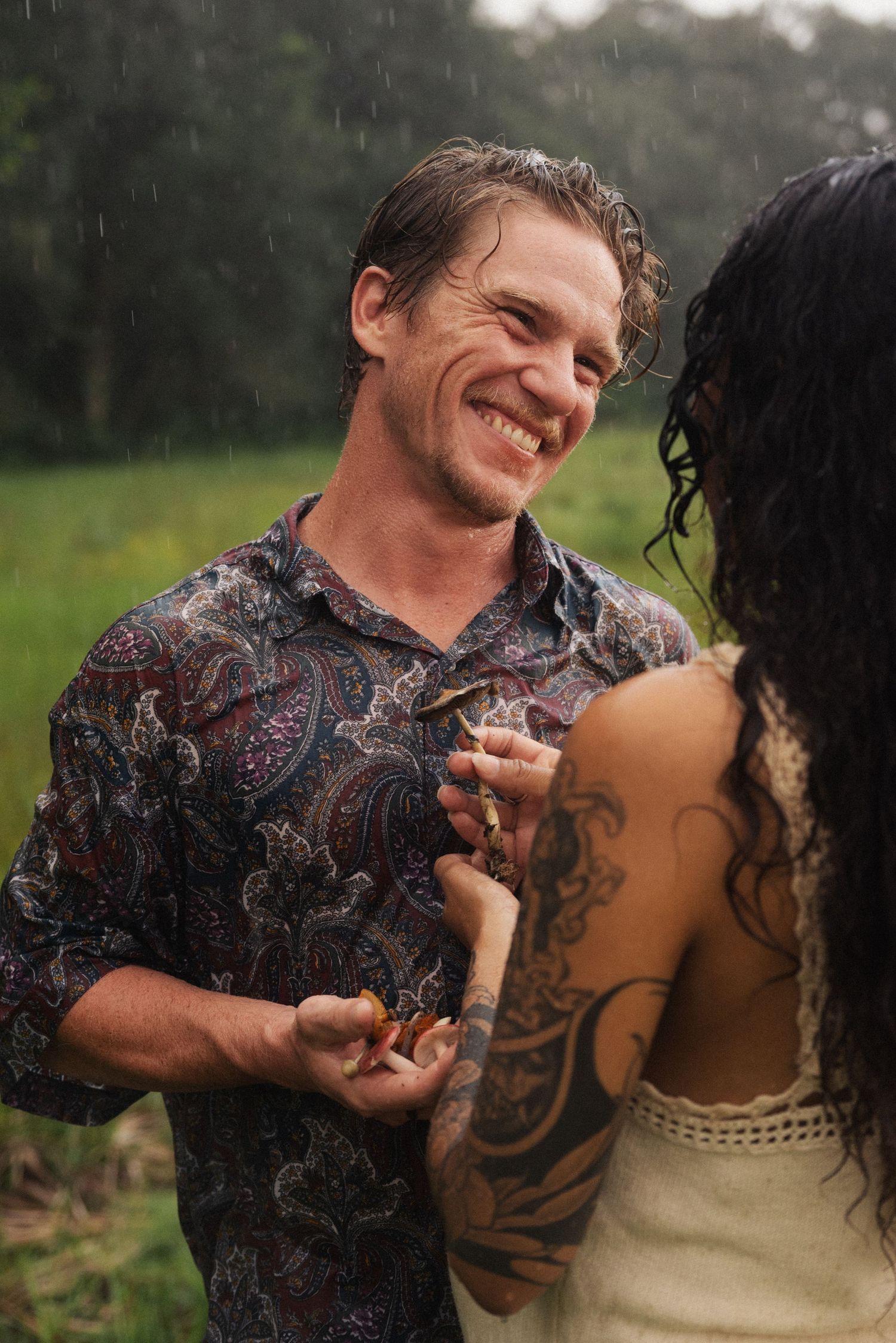 Couple laughing and playing together in a field wearing casual attire.