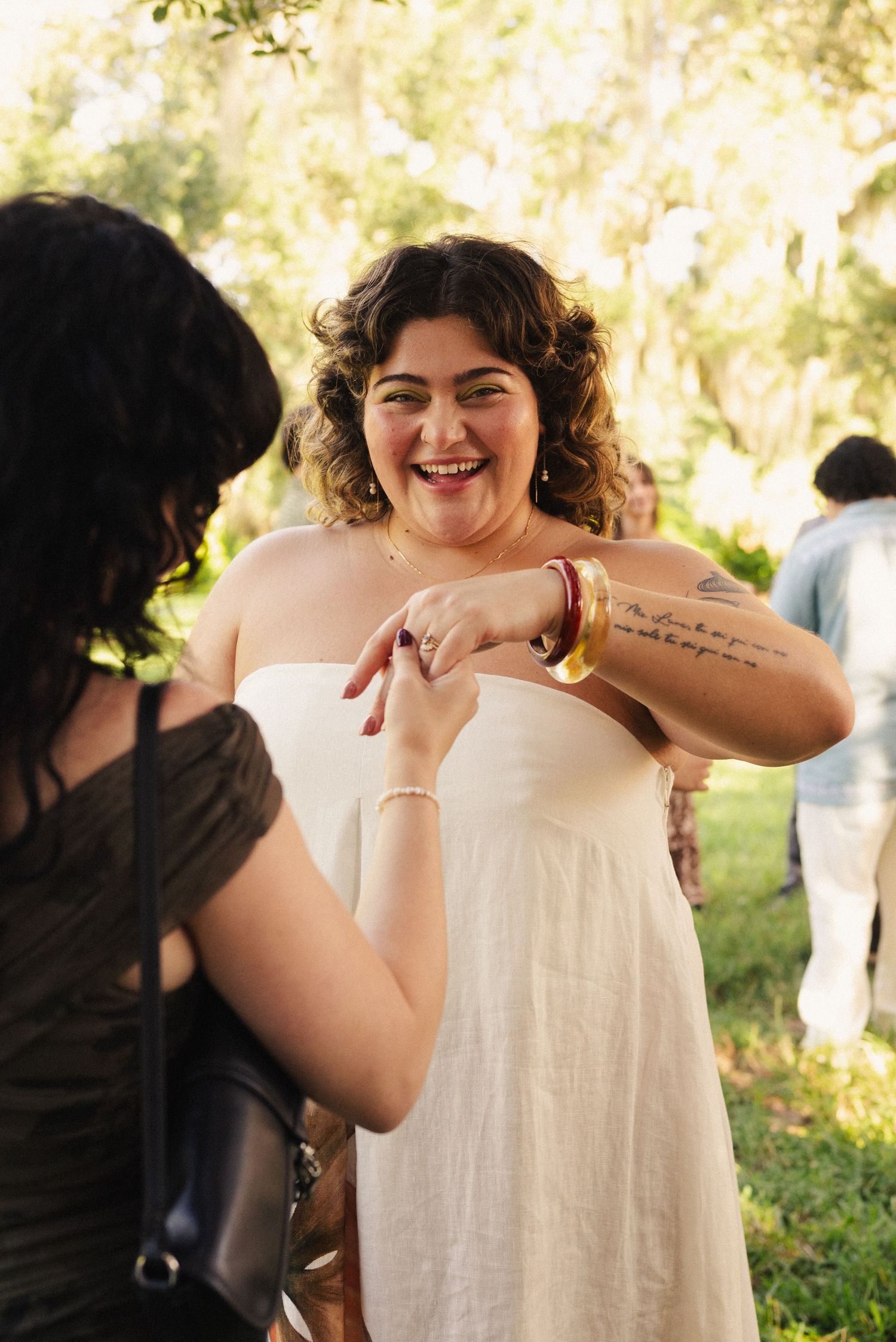 Person in white dress laughs joyfully during outdoor wedding celebration.