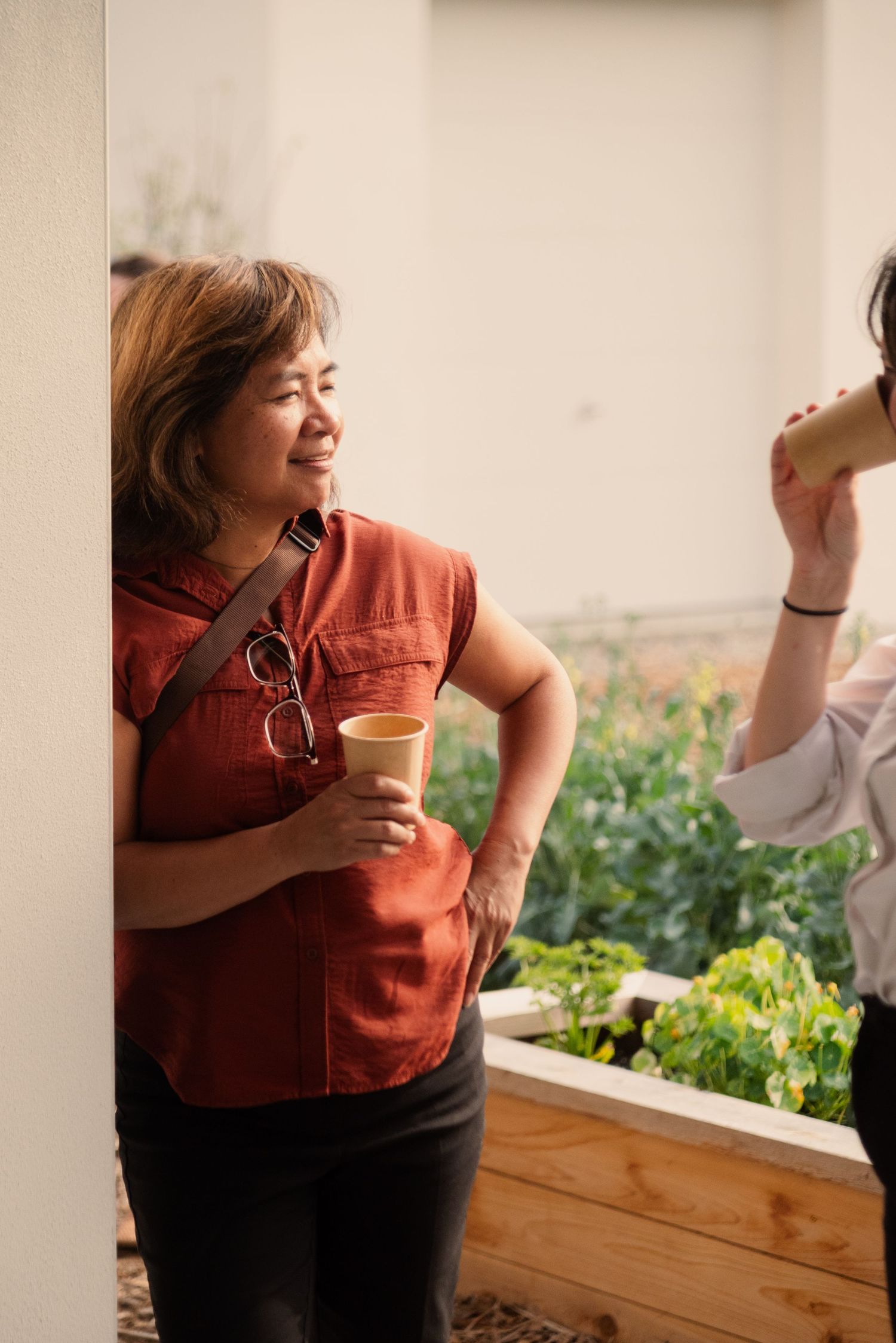 Person in an orange shirt holding a beverage cup near a garden planter.