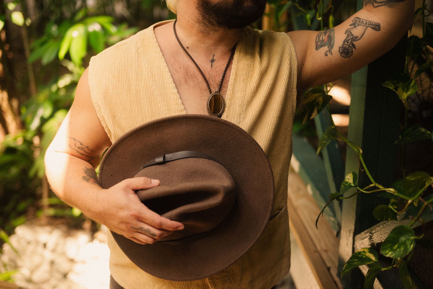 Person holding a brown hat while posing against natural foliage.