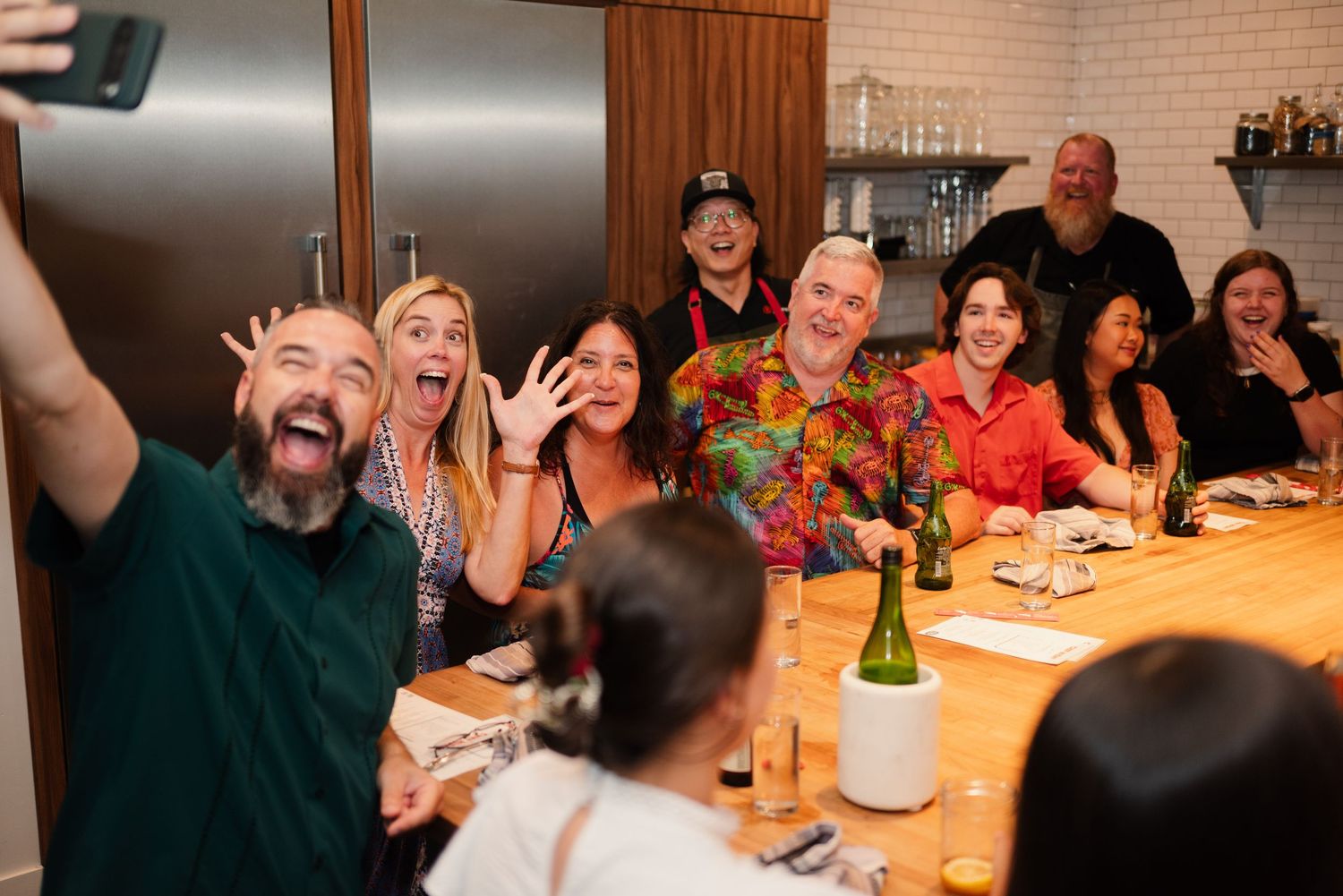 Group dining and socializing at a long wooden table in a restaurant setting.