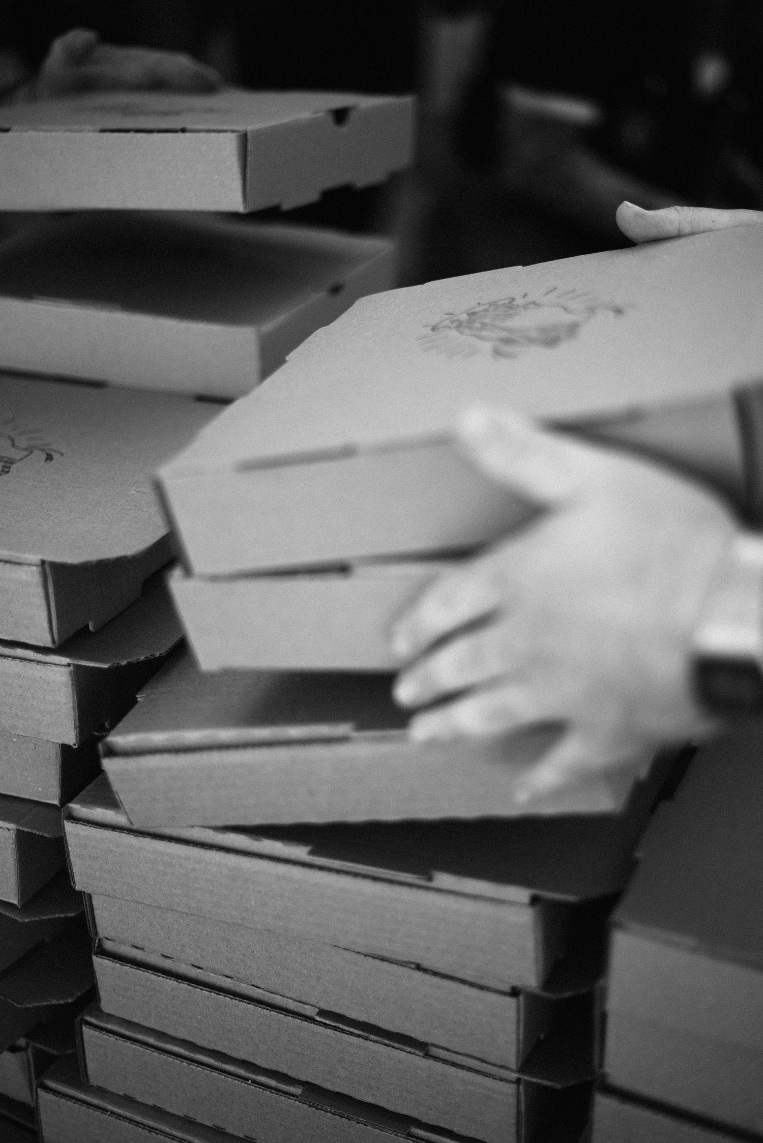 Hands sorting through stacks of cardboard boxes and papers on dark surface.