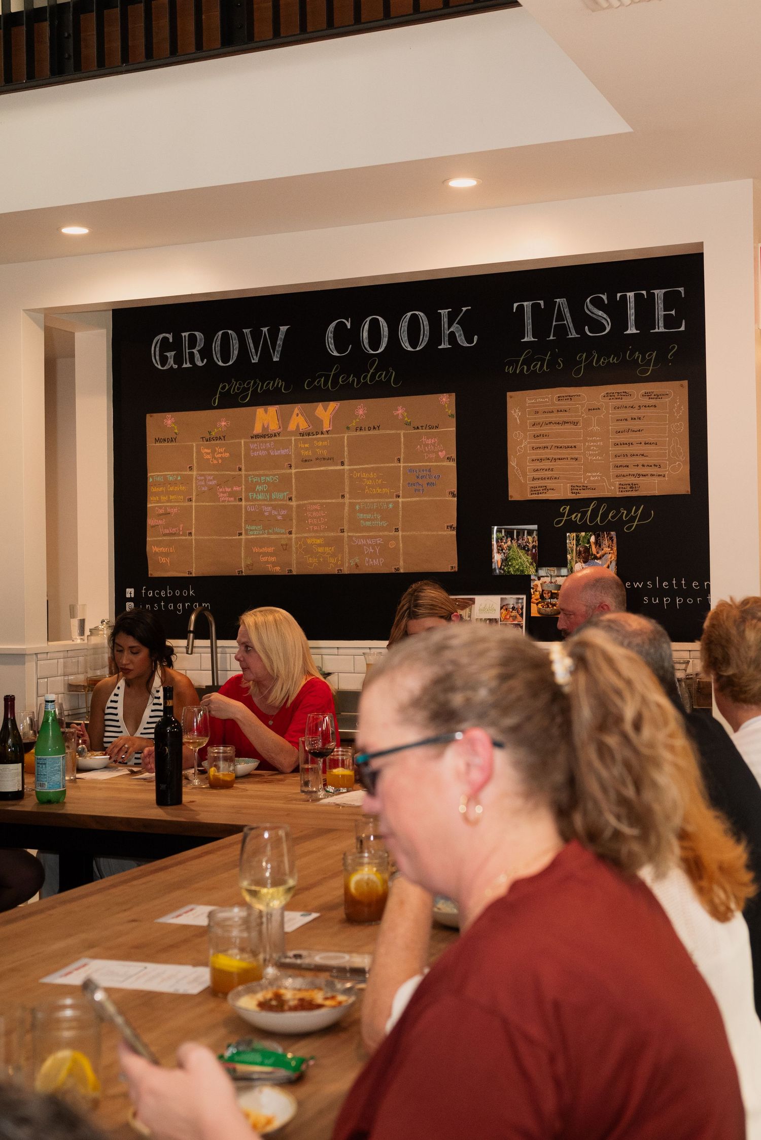 Restaurant interior with wooden counter seating and 'Grow Cook Taste' text displayed on dark wall.