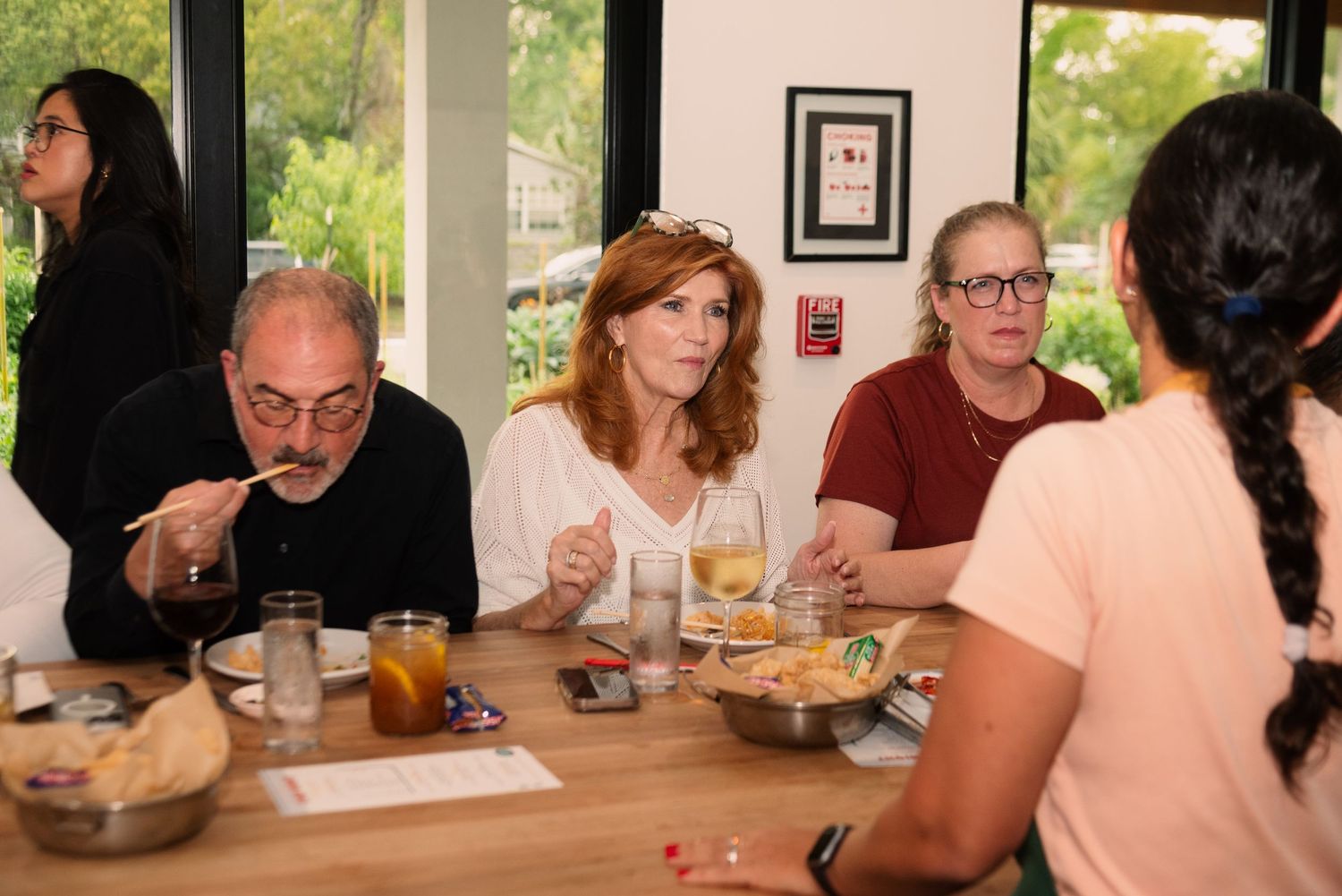 Diners enjoying a casual meal at wooden table in bright restaurant space with windows.