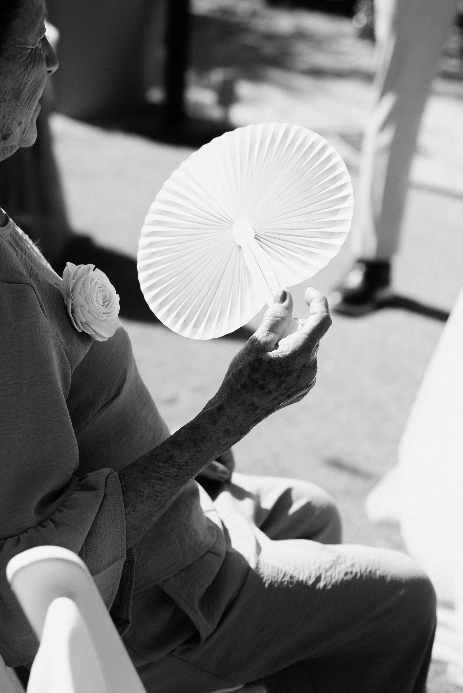 Person holding a white folding hand fan in black and white photography.