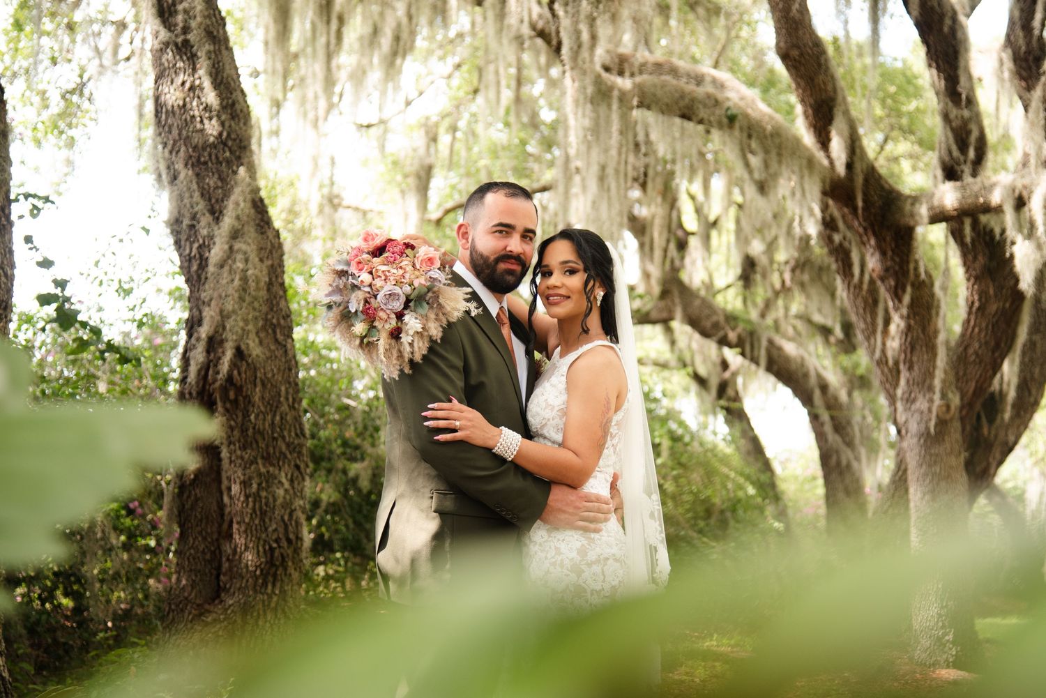 A romantic wedding portrait under Spanish moss trees with pink floral bouquet.