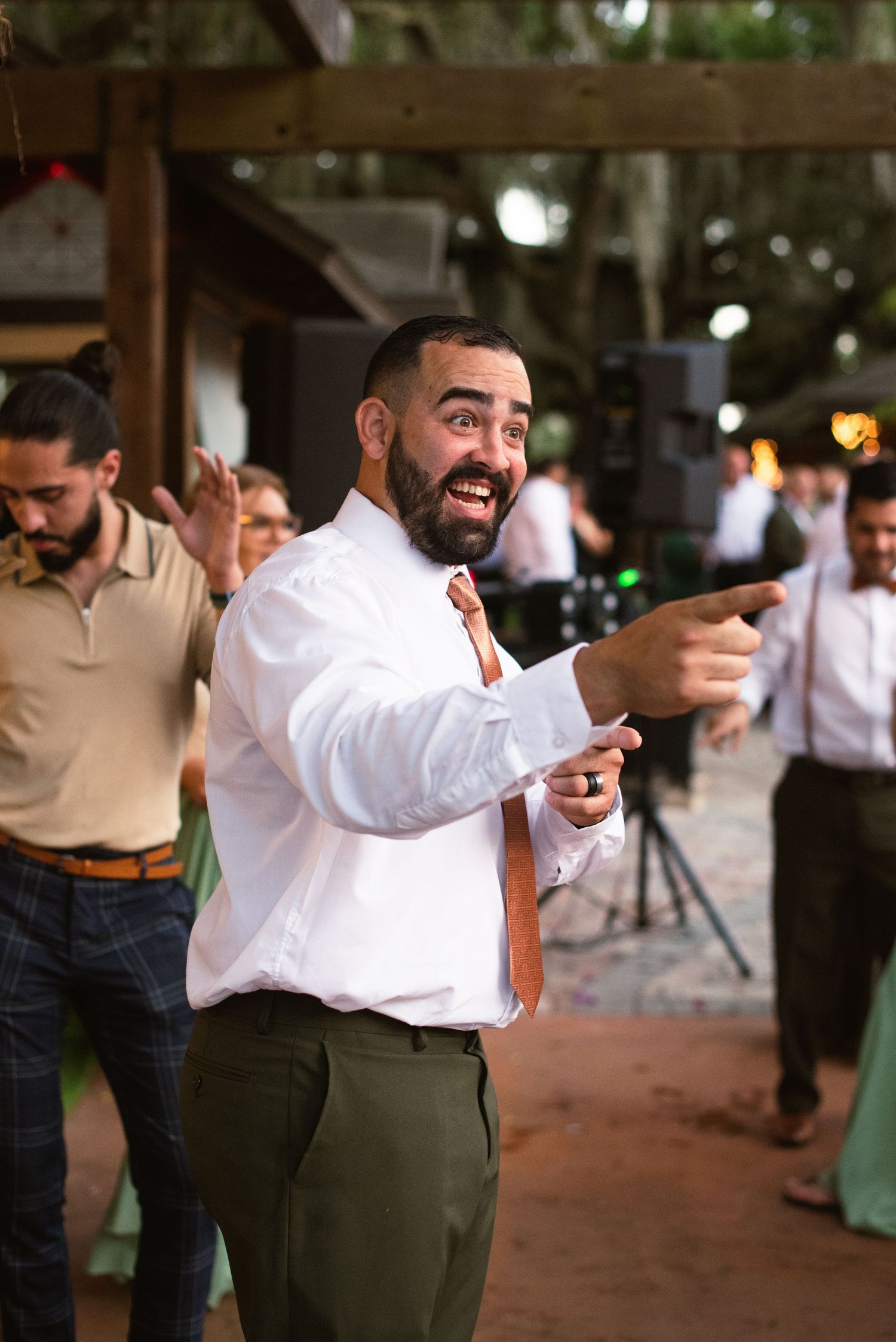 Wedding party celebrates with dancing and laughter at an outdoor venue.