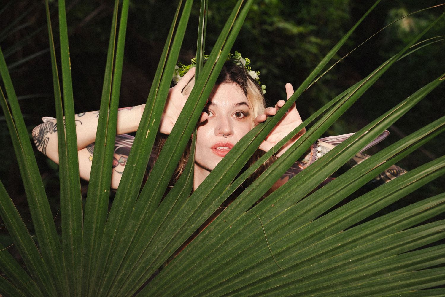 Dreamy portrait through palm fronds with flower crown and natural lighting.