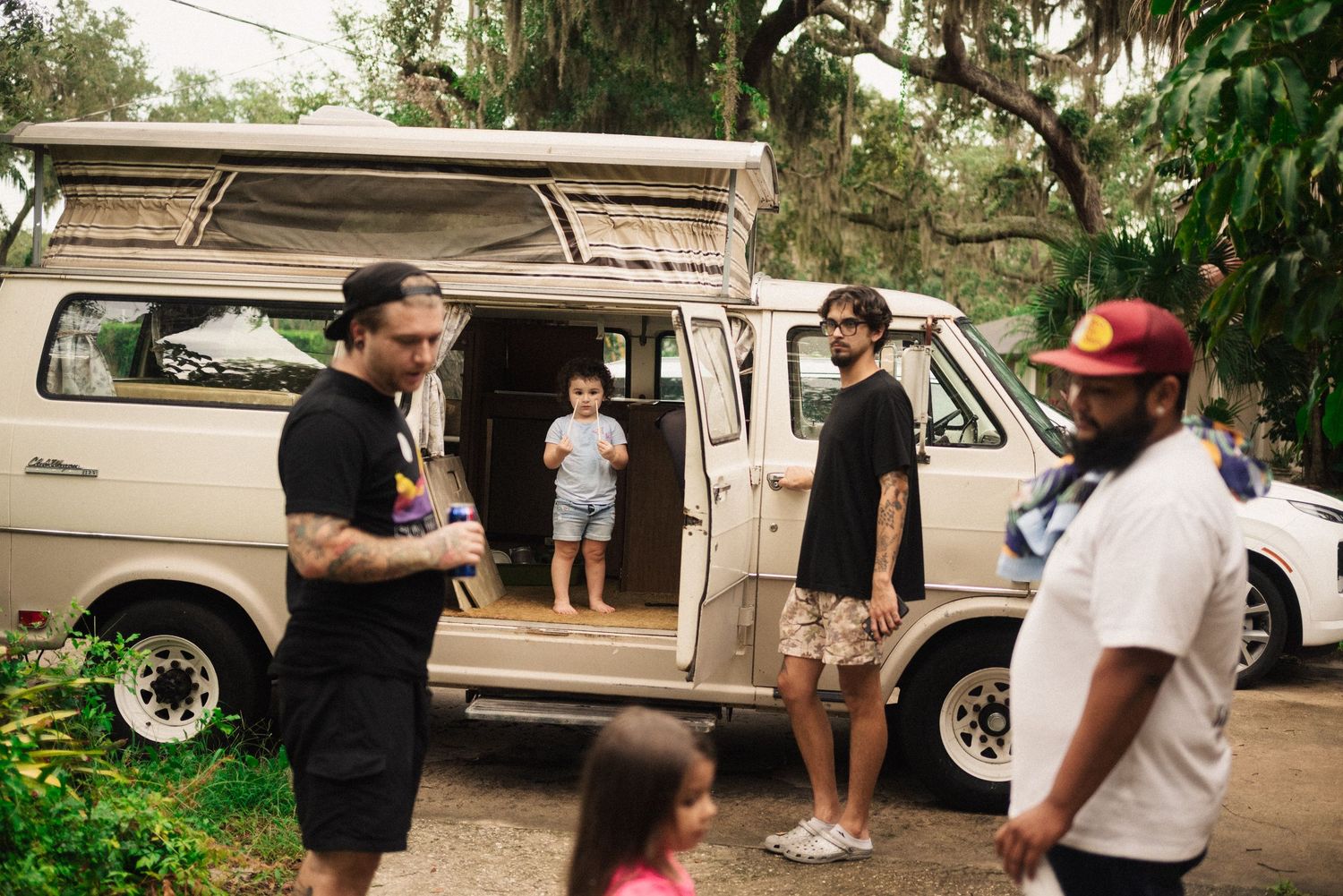 People gathered around parked vans and vehicles in an outdoor setting.