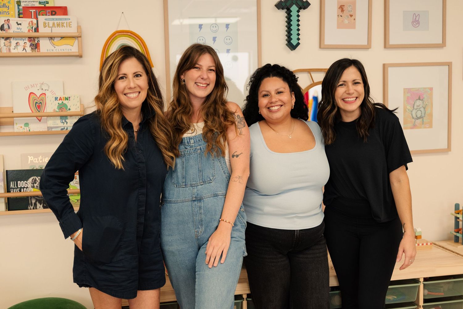 Group photo of staff members in a cheerful classroom decorated with framed artwork.