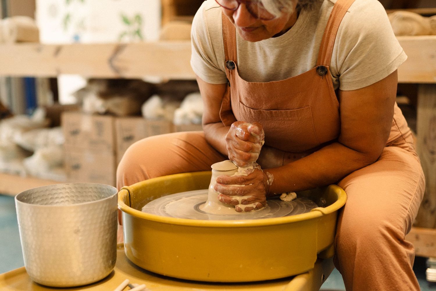 Ceramicist shapes clay on yellow pottery wheel in studio workspace.
