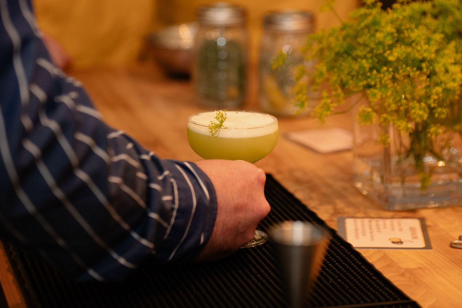 Close-up of cocktail ingredients and garnishes on a wooden surface with glass jars in the background.