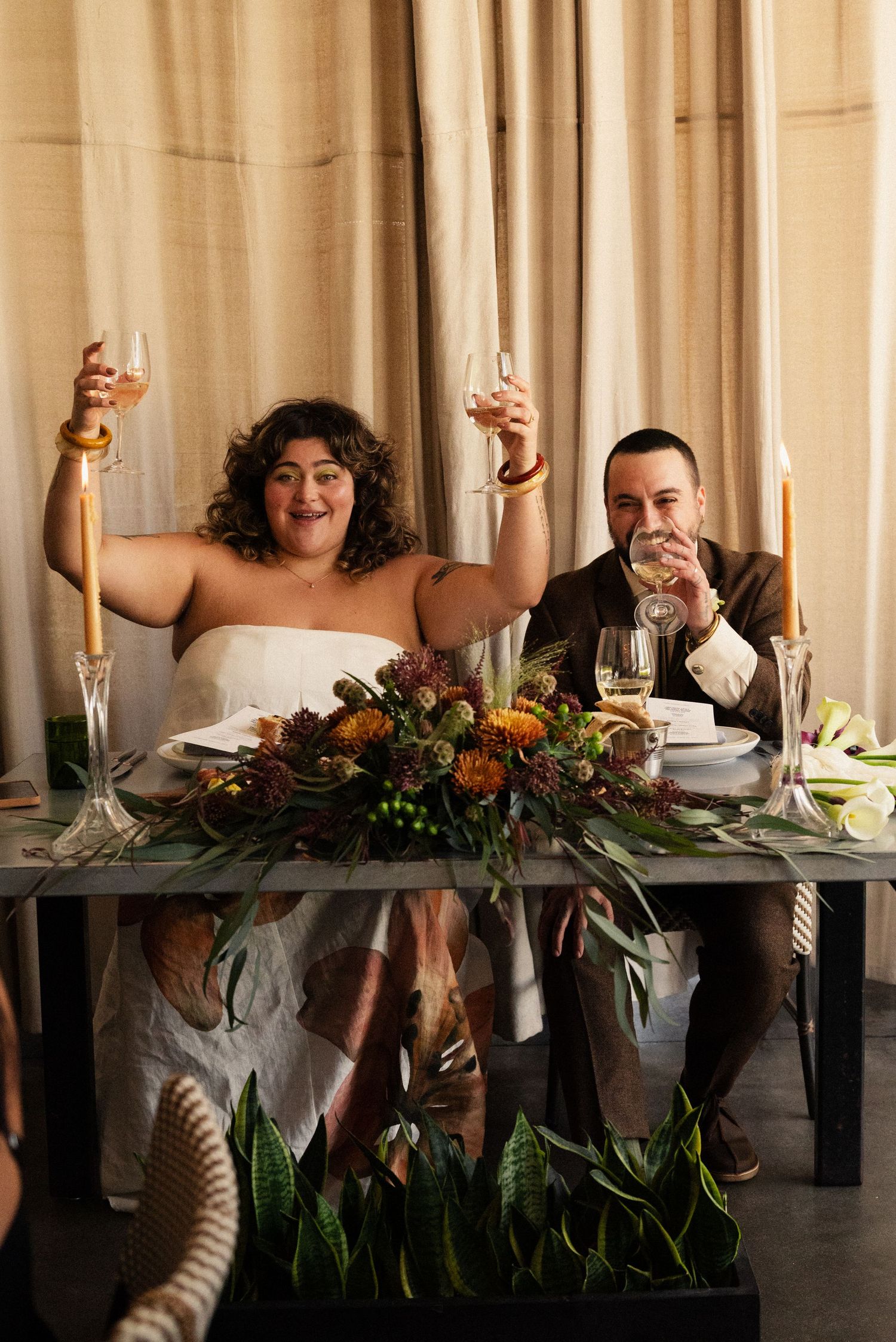 A couple toasting with champagne at their wedding reception table adorned with floral centerpieces.
