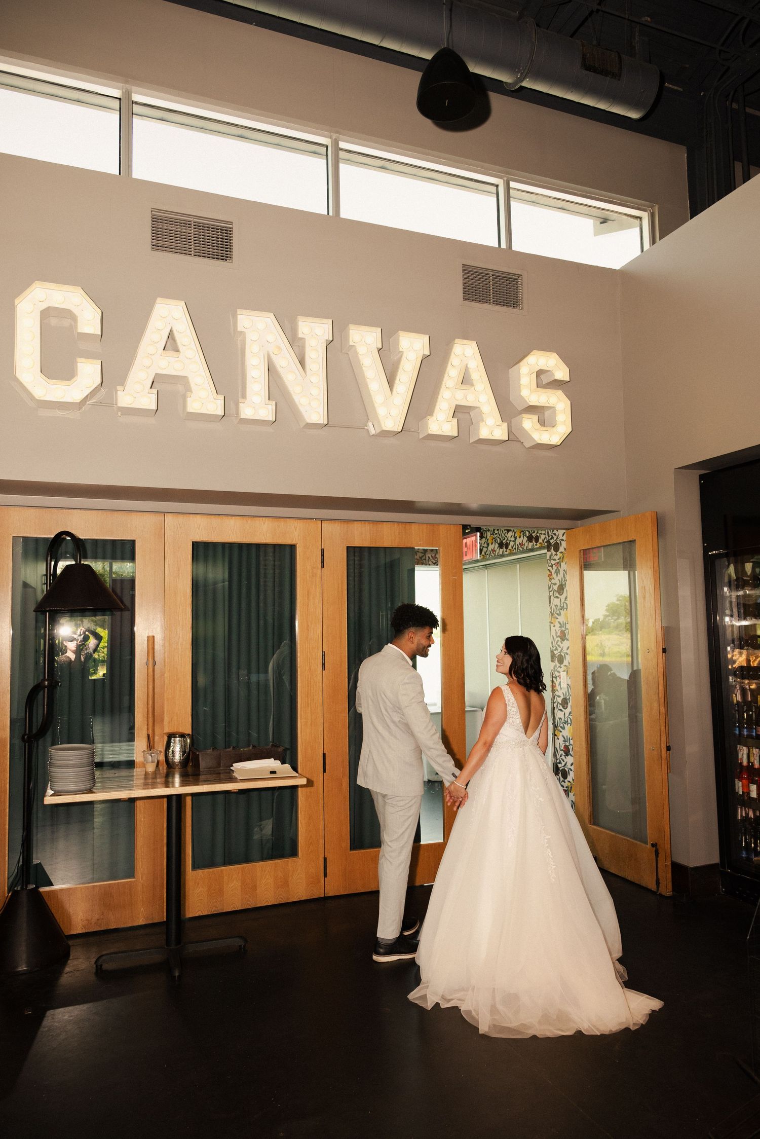 Wedding couple poses in silhouette inside venue with 'CANVAS' signage visible.