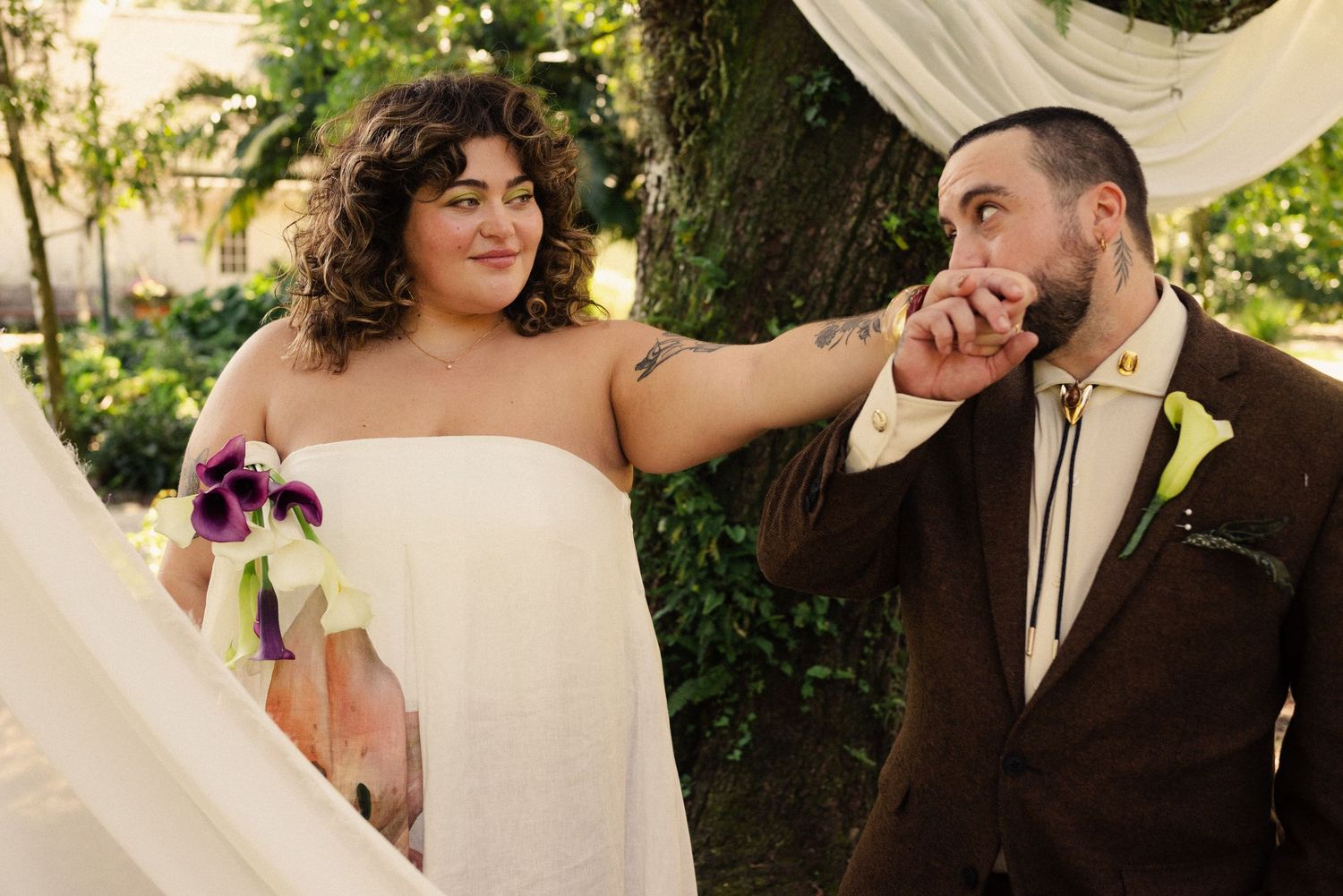 A romantic wedding moment captured under white fabric draping in a garden setting.