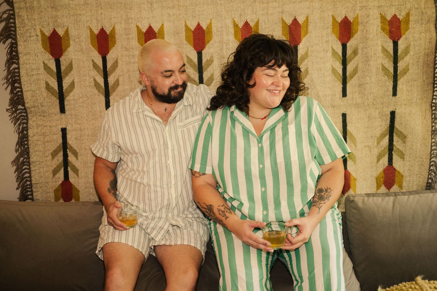 Two people in coordinated striped outfits relaxing on a gray couch.