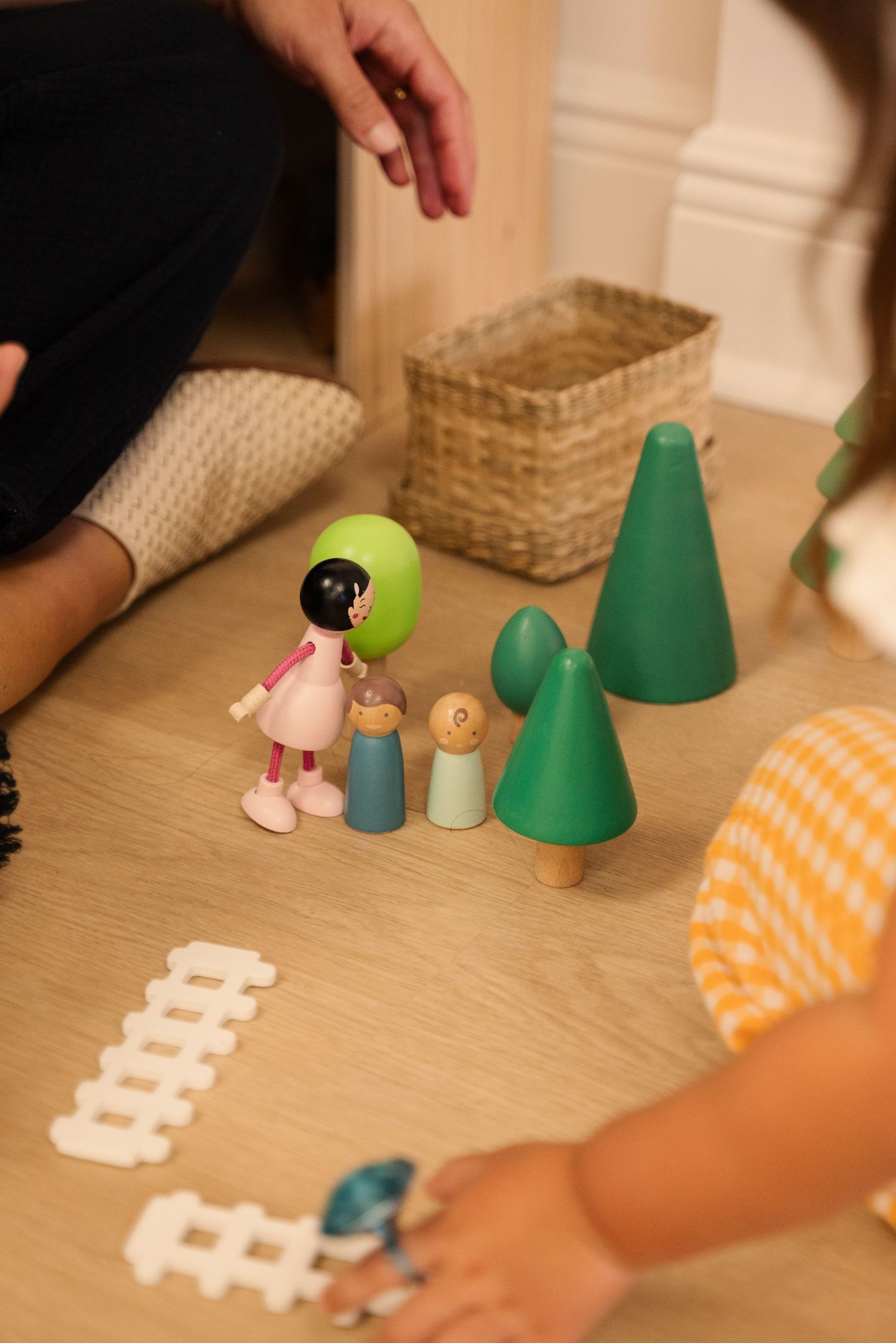 Wooden toys and miniature trees arranged on a light wooden floor.