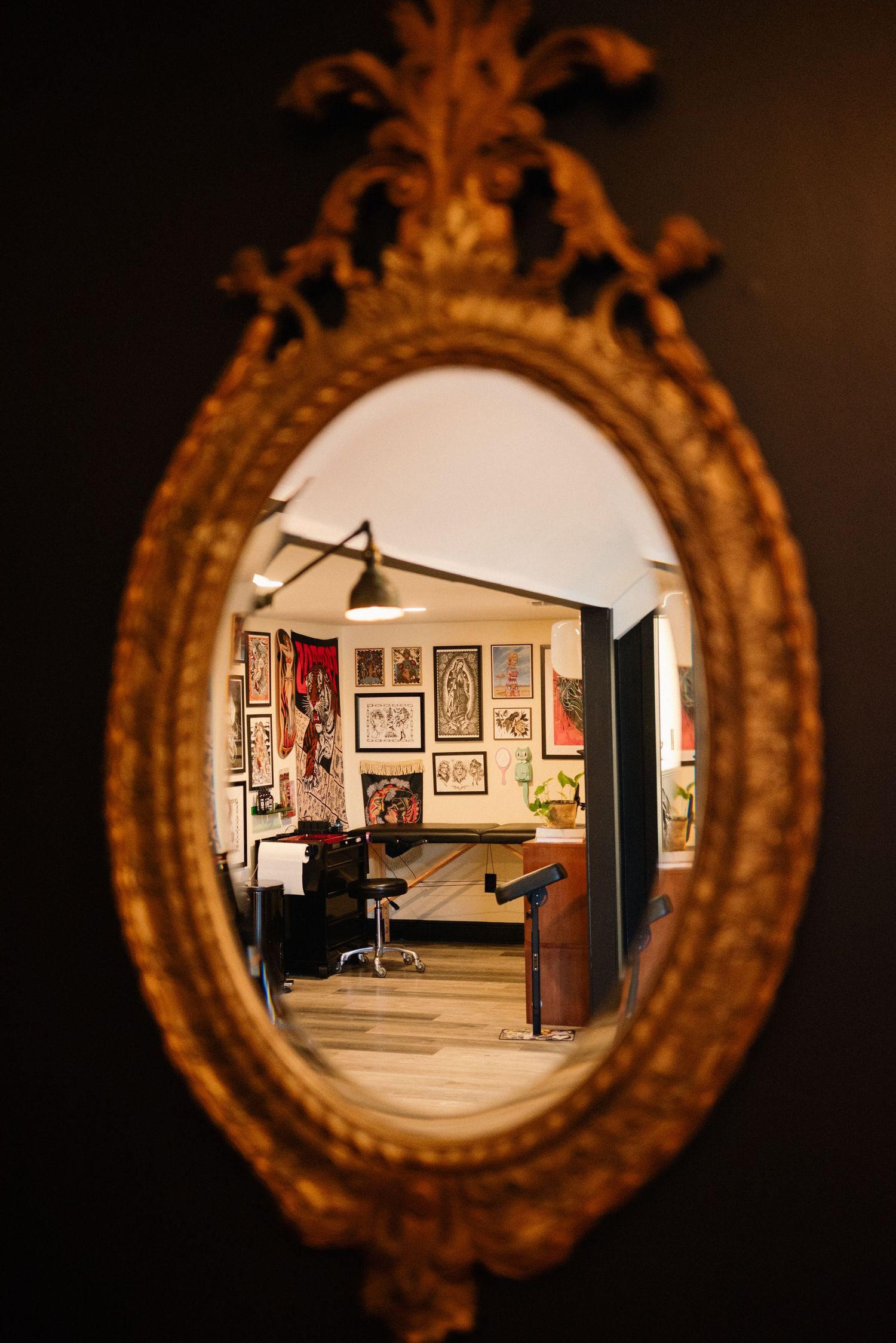 Ornate gold mirror reflection shows a tattoo studio interior with artwork on walls.