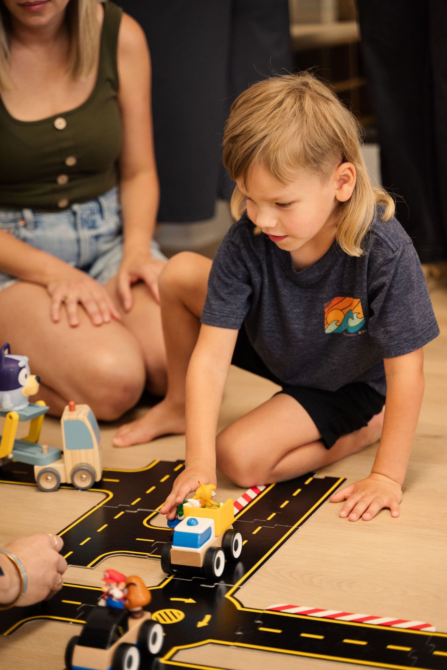 Playing with toy cars on a black road playmat on the floor.