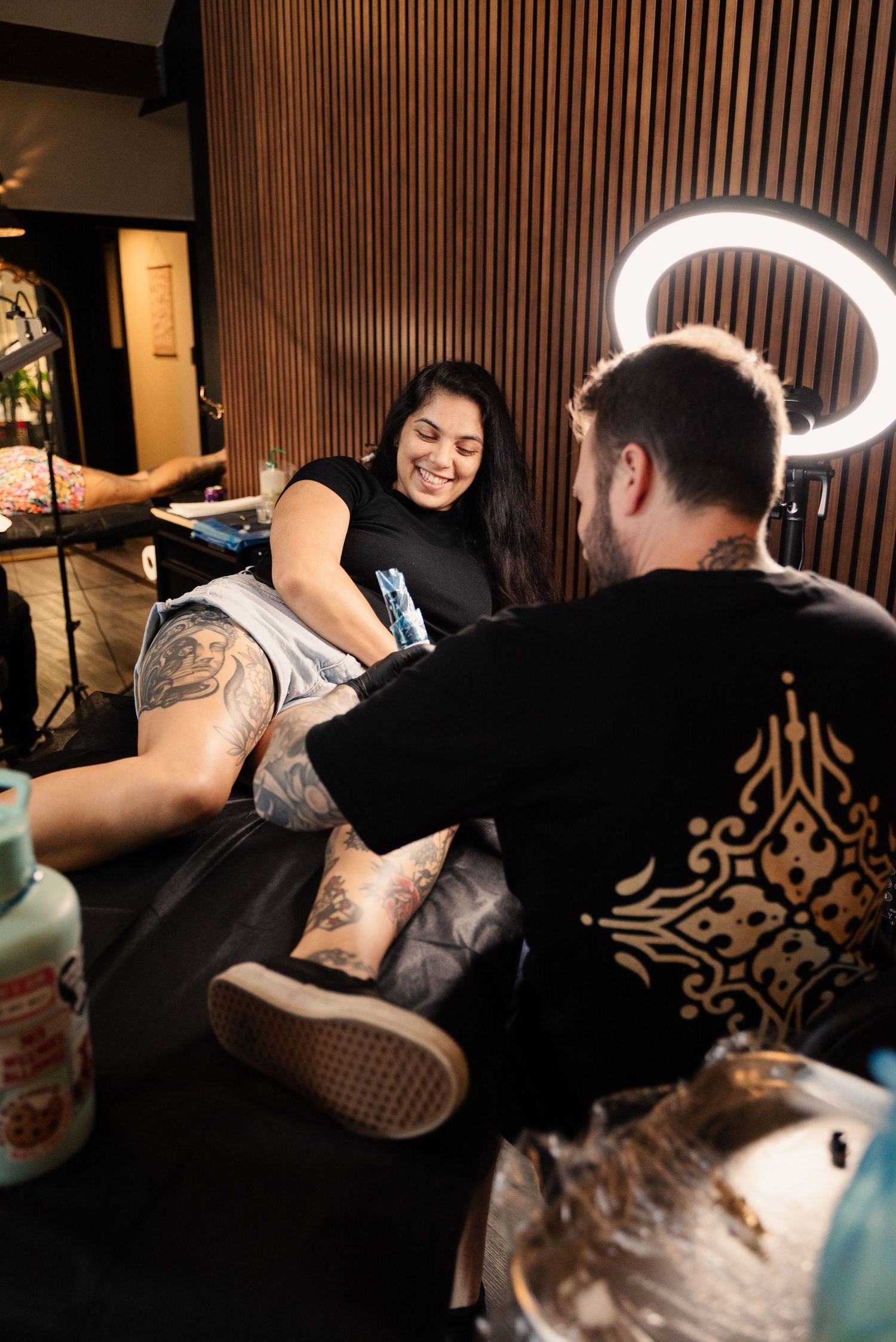 Tattoo session in progress with artist working in a wood-paneled studio space.