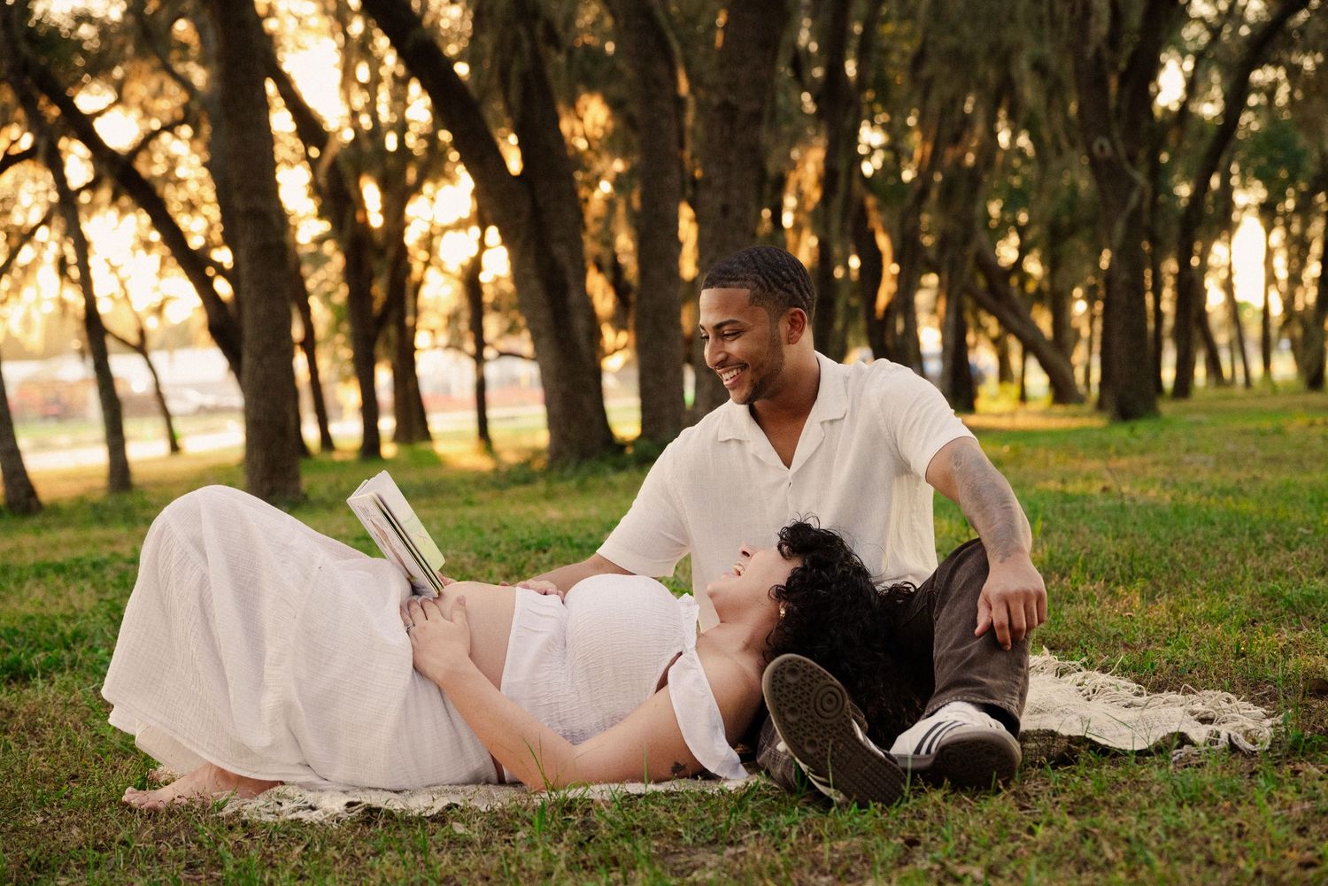 A couple relaxes on a blanket in a grassy field at sunset.