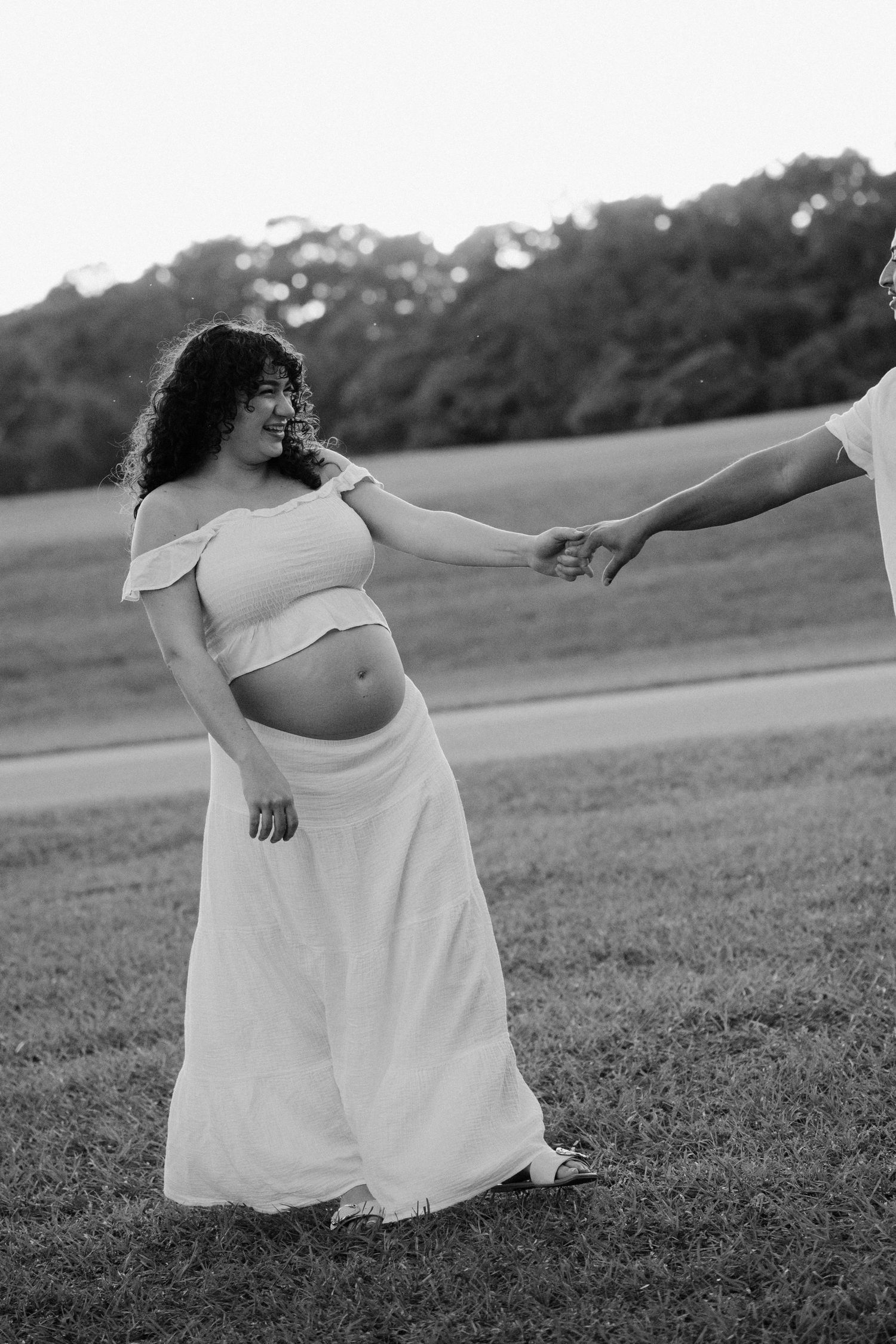 Black and white maternity photos capture couple's playful moments in open field.
