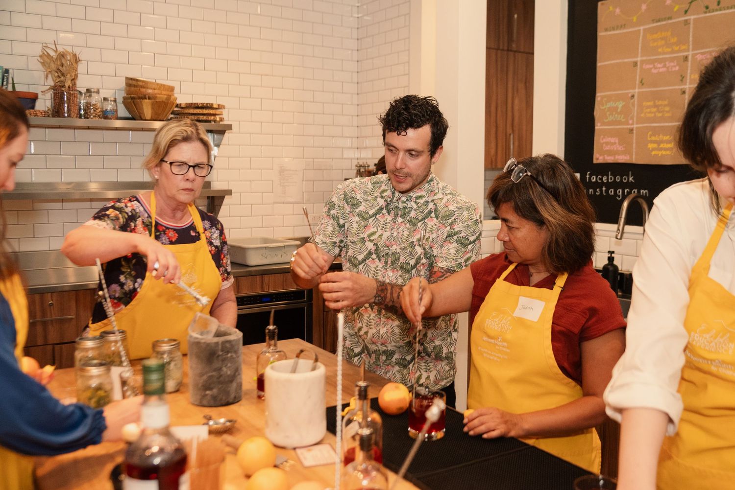 Students in yellow aprons practicing mixology techniques at a bar station.