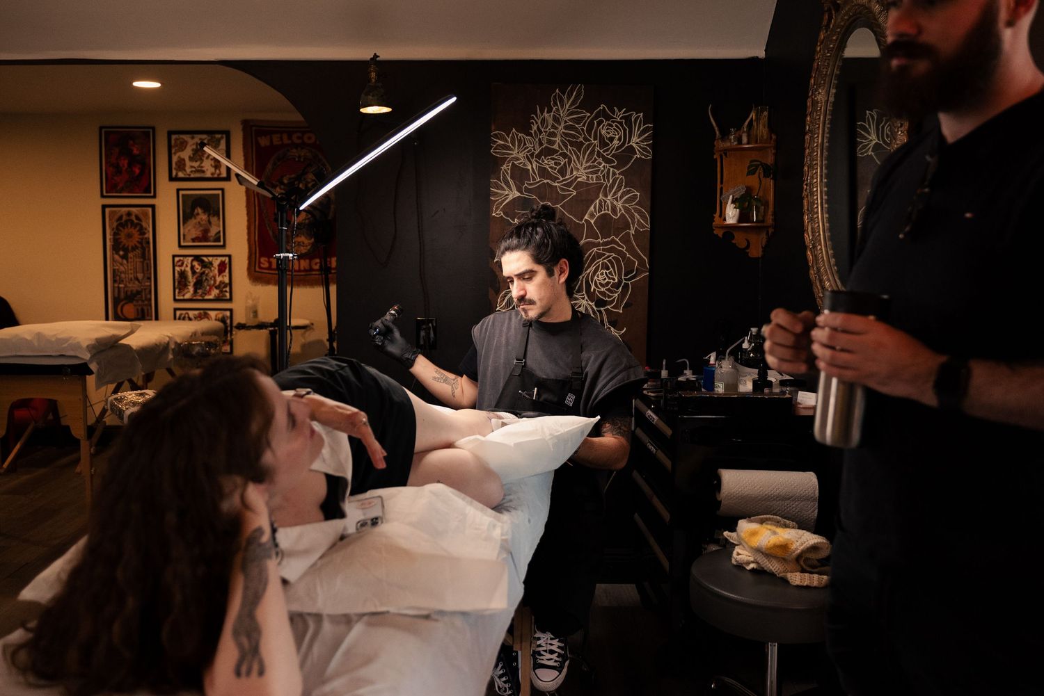 Tattoo artists at work in a dimly lit studio space with professional equipment.