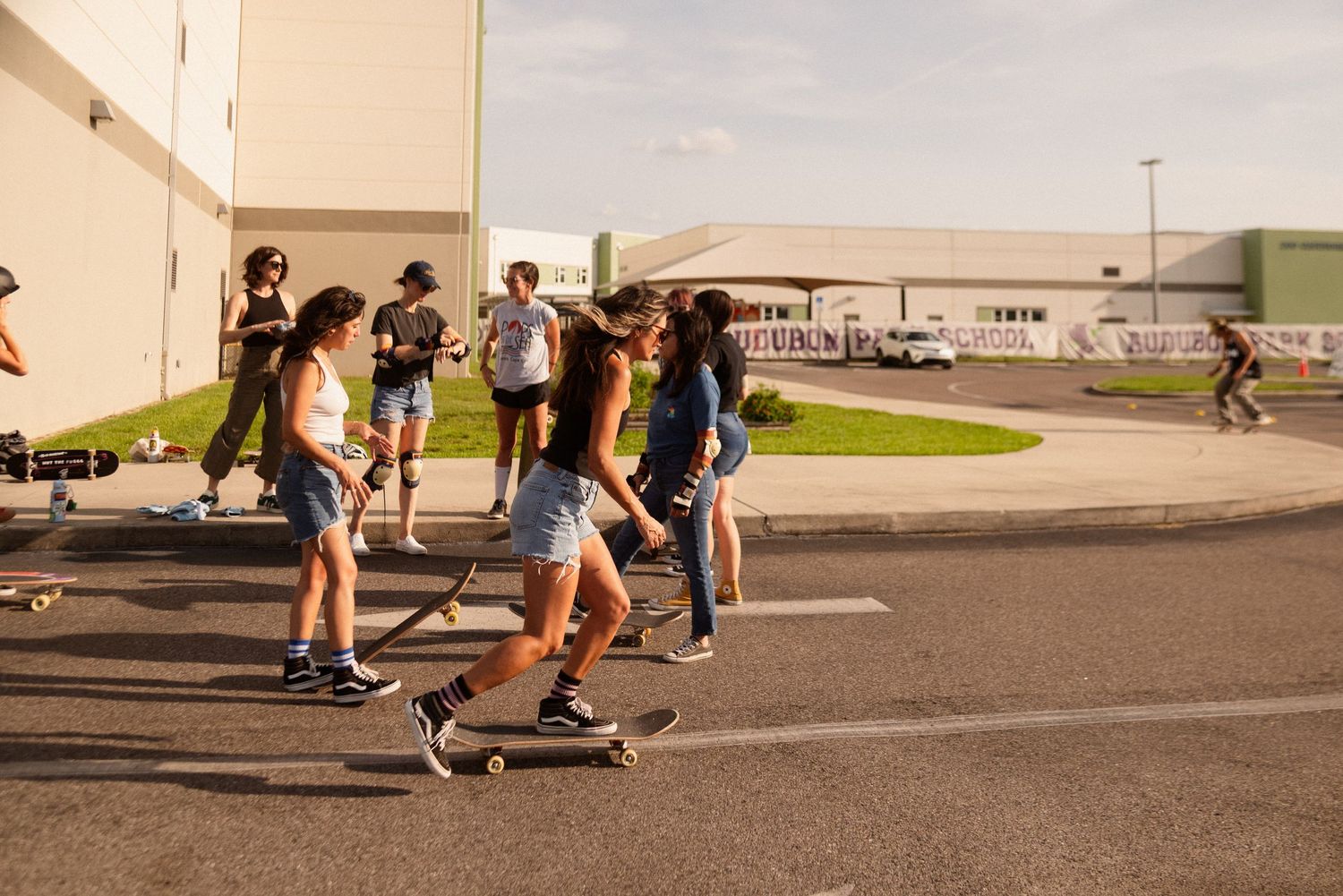 People skateboarding across an empty parking lot during sunset.