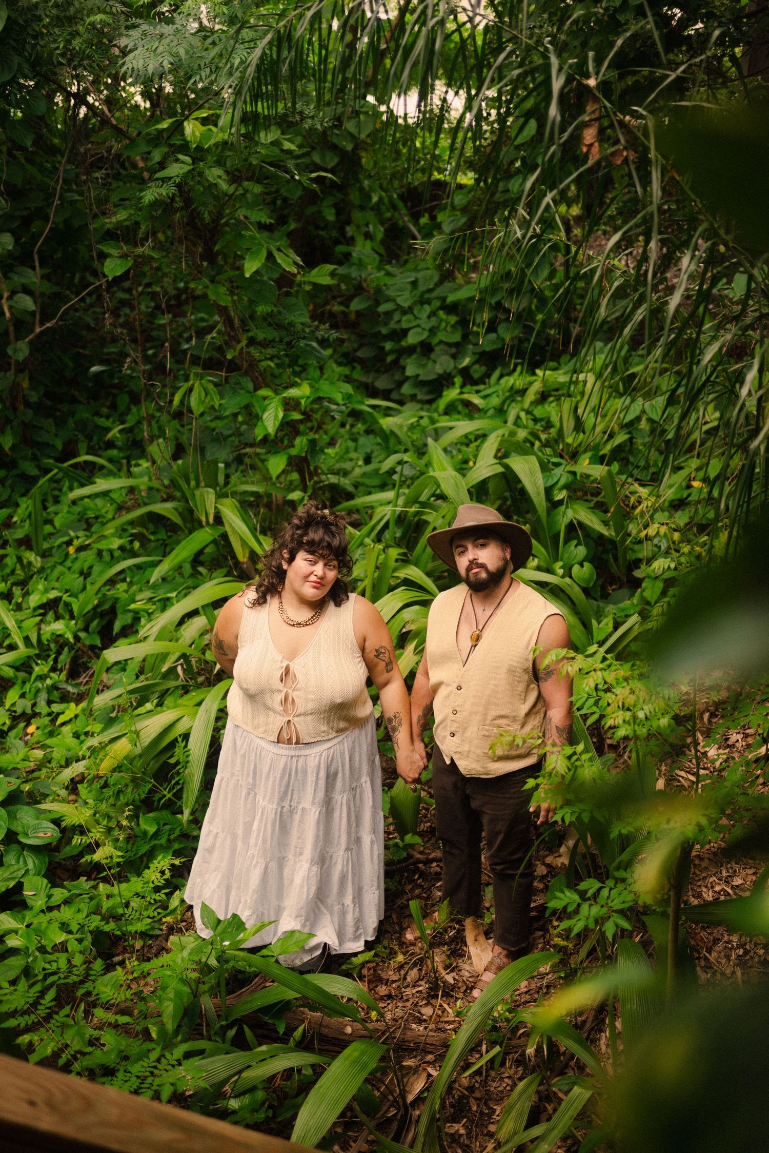 Couple poses together in natural garden setting wearing coordinated earth-toned outfits.