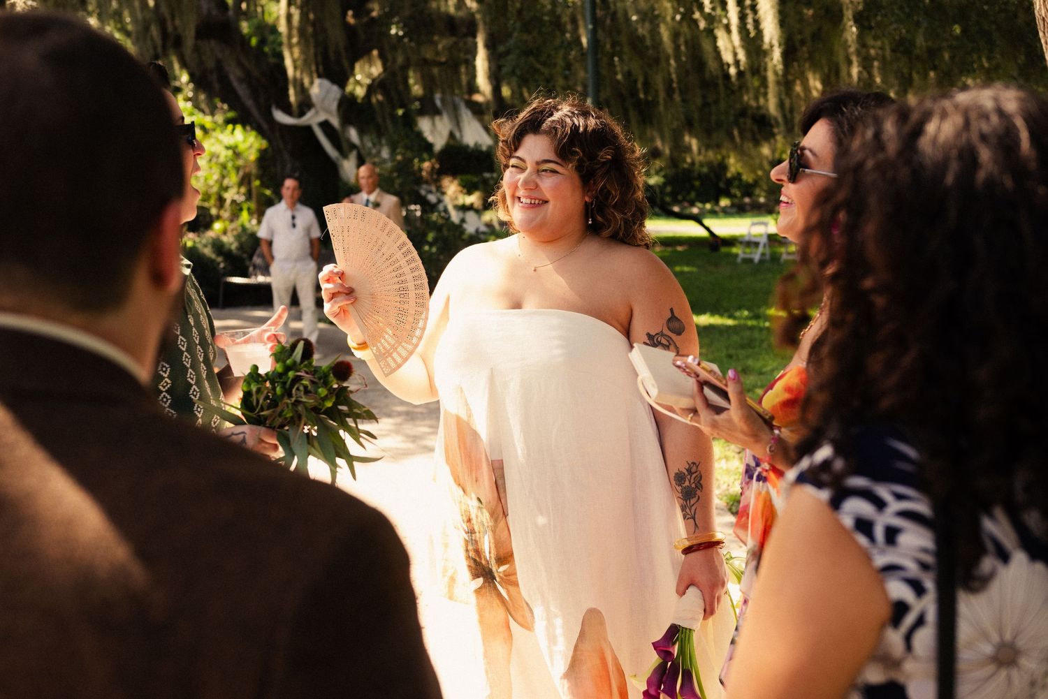 Wedding guests gather outdoors under Spanish moss-covered trees for a ceremony.