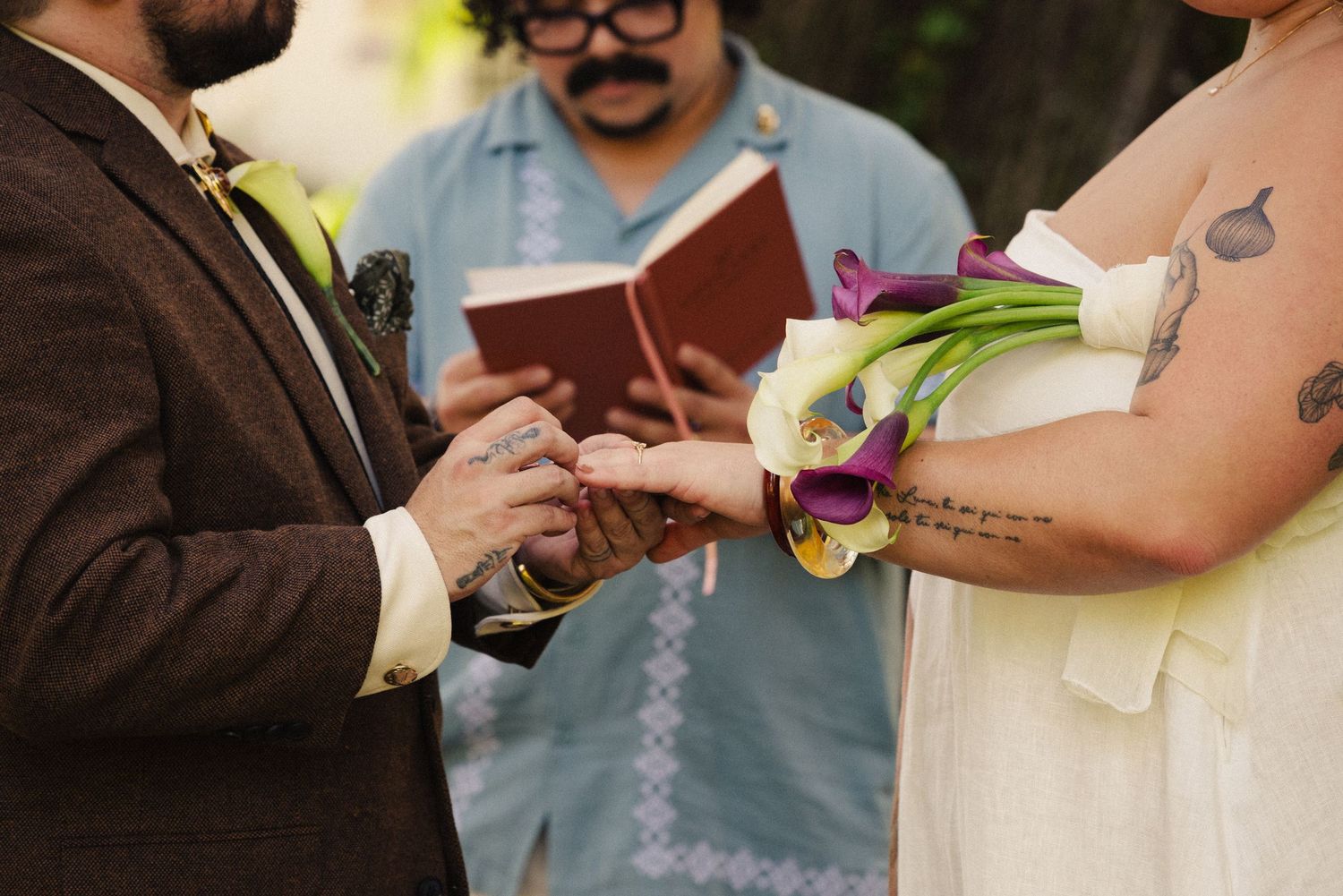 Wedding ceremony participants exchange vows while holding books outdoors.