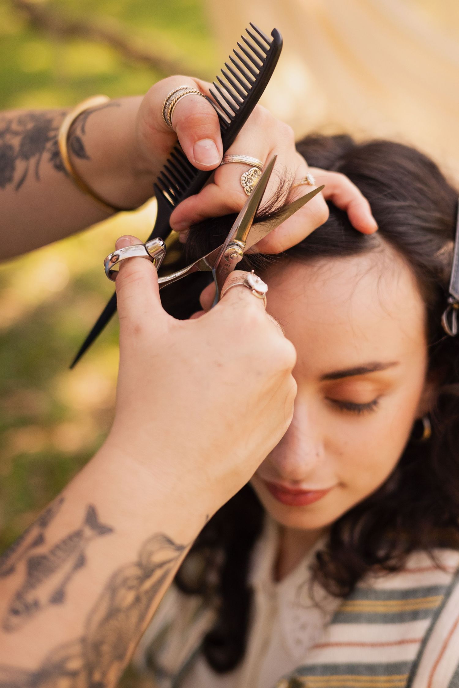 Close-up of hair styling session with comb and scissors against natural outdoor backdrop.