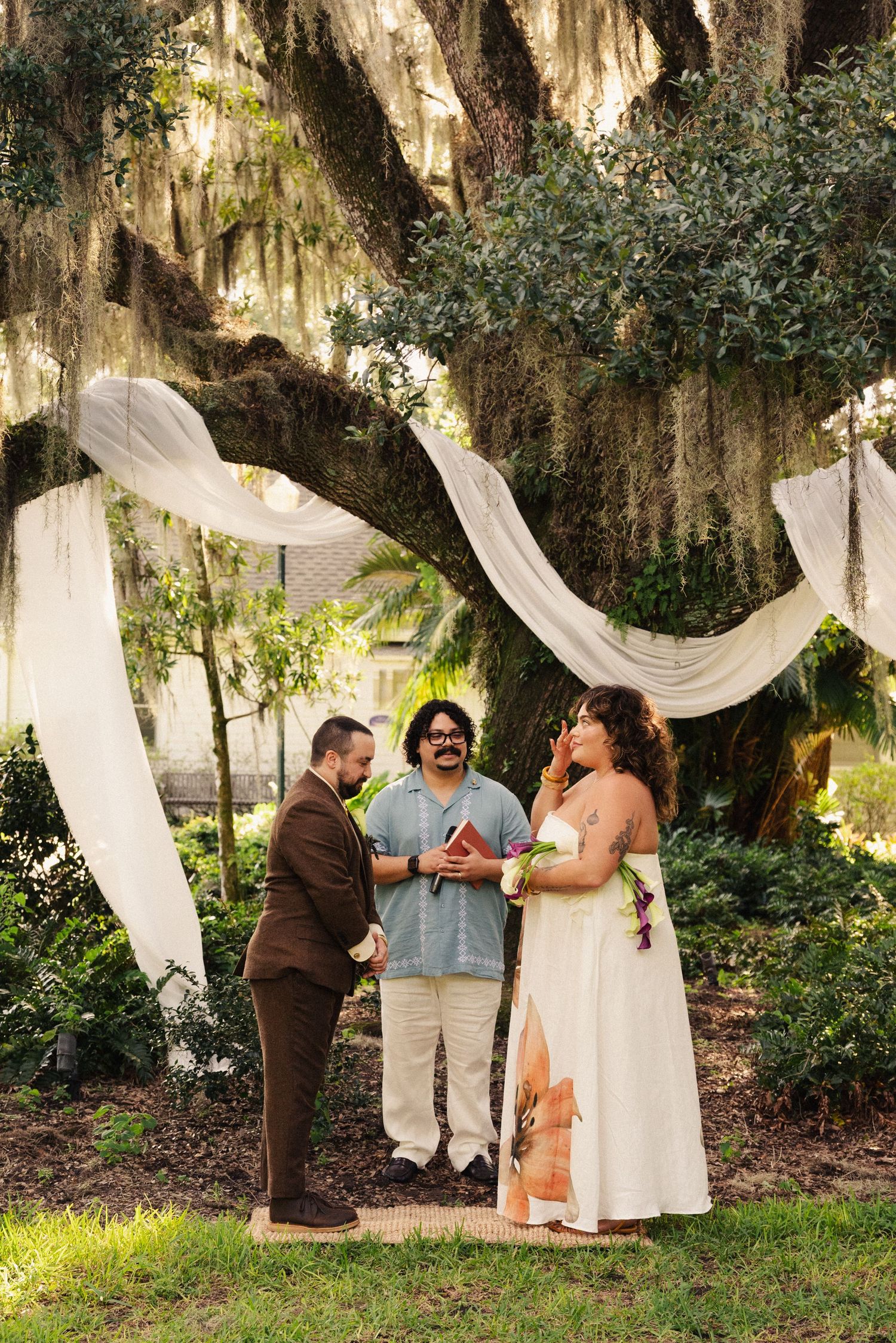 Outdoor wedding ceremony under draped white fabric and Spanish moss covered trees.