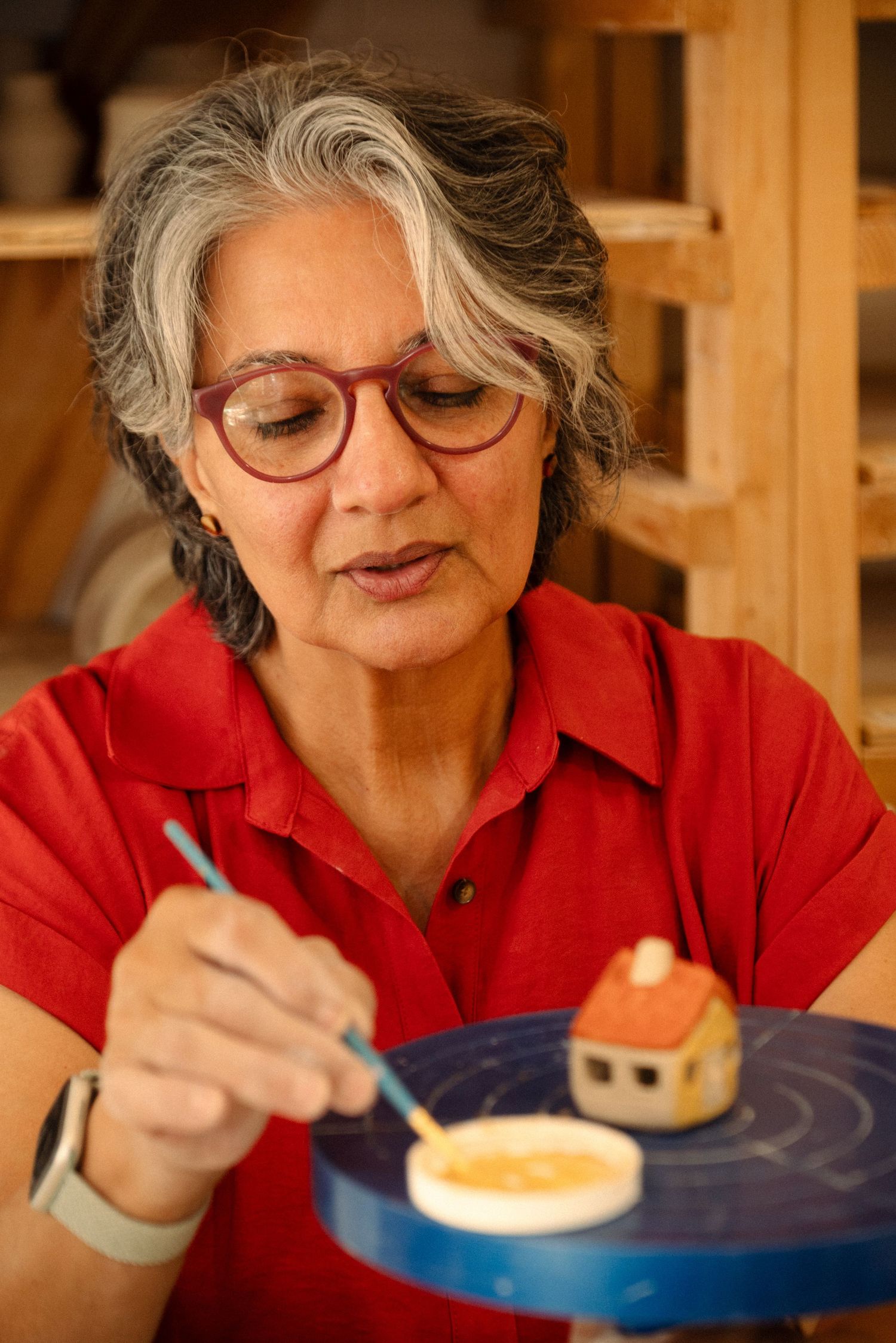 Artist carefully detailing a small ceramic house on a blue wheel.
