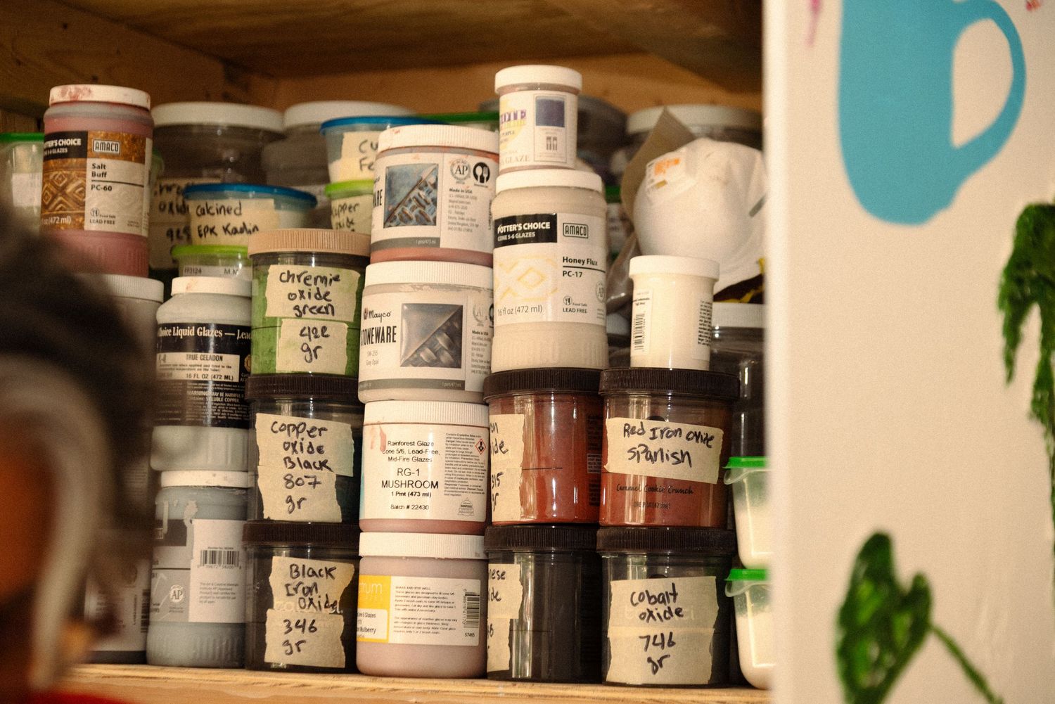 Rows of labeled pottery glazes and supplies stored on wooden shelves.