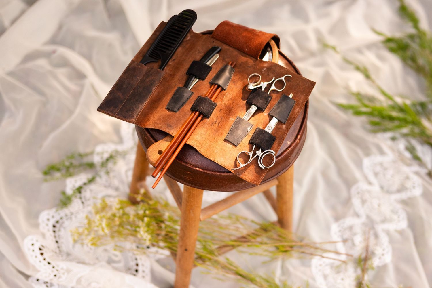 Antique leather tool case with metallic implements arranged in a row on white fabric.