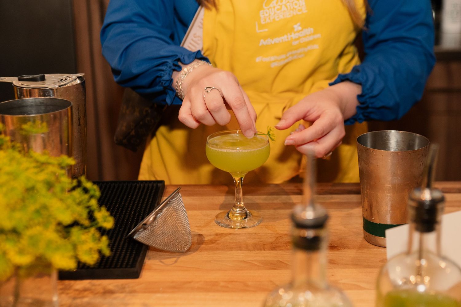 Hands pouring mixed drinks into cocktail glasses during a bartending class.