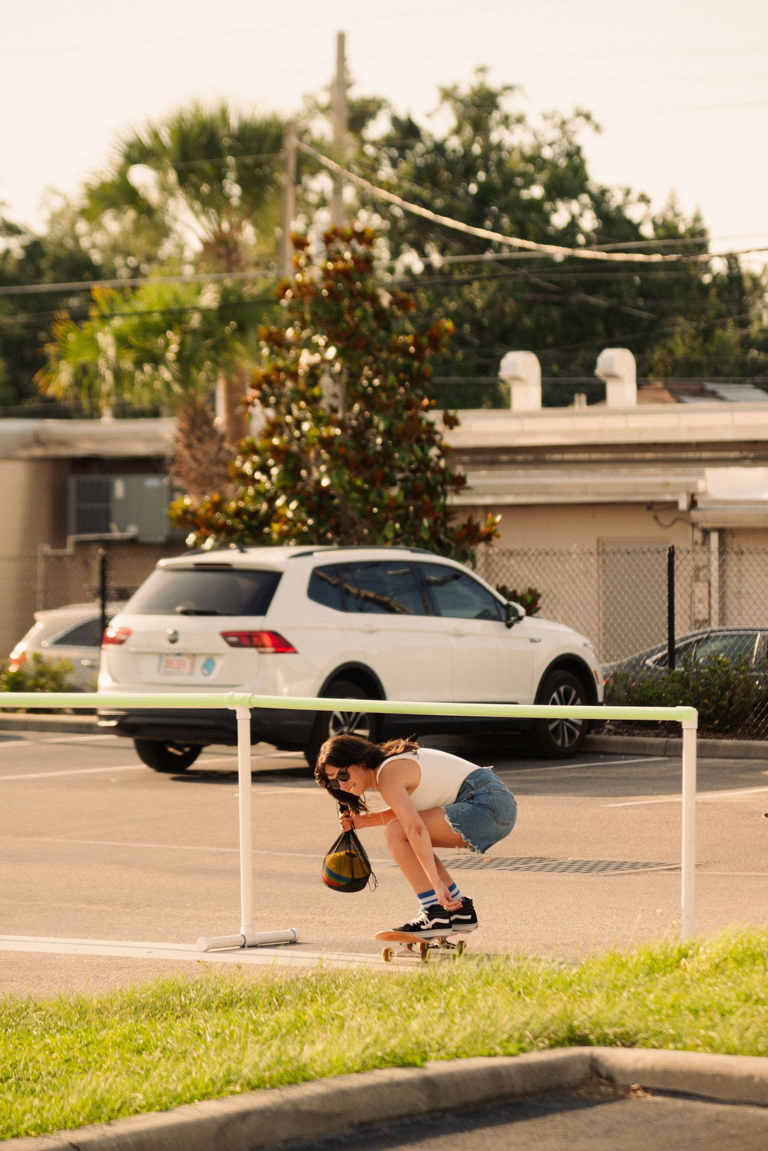 Skateboarder performing an ollie over a white barrier in a parking lot.