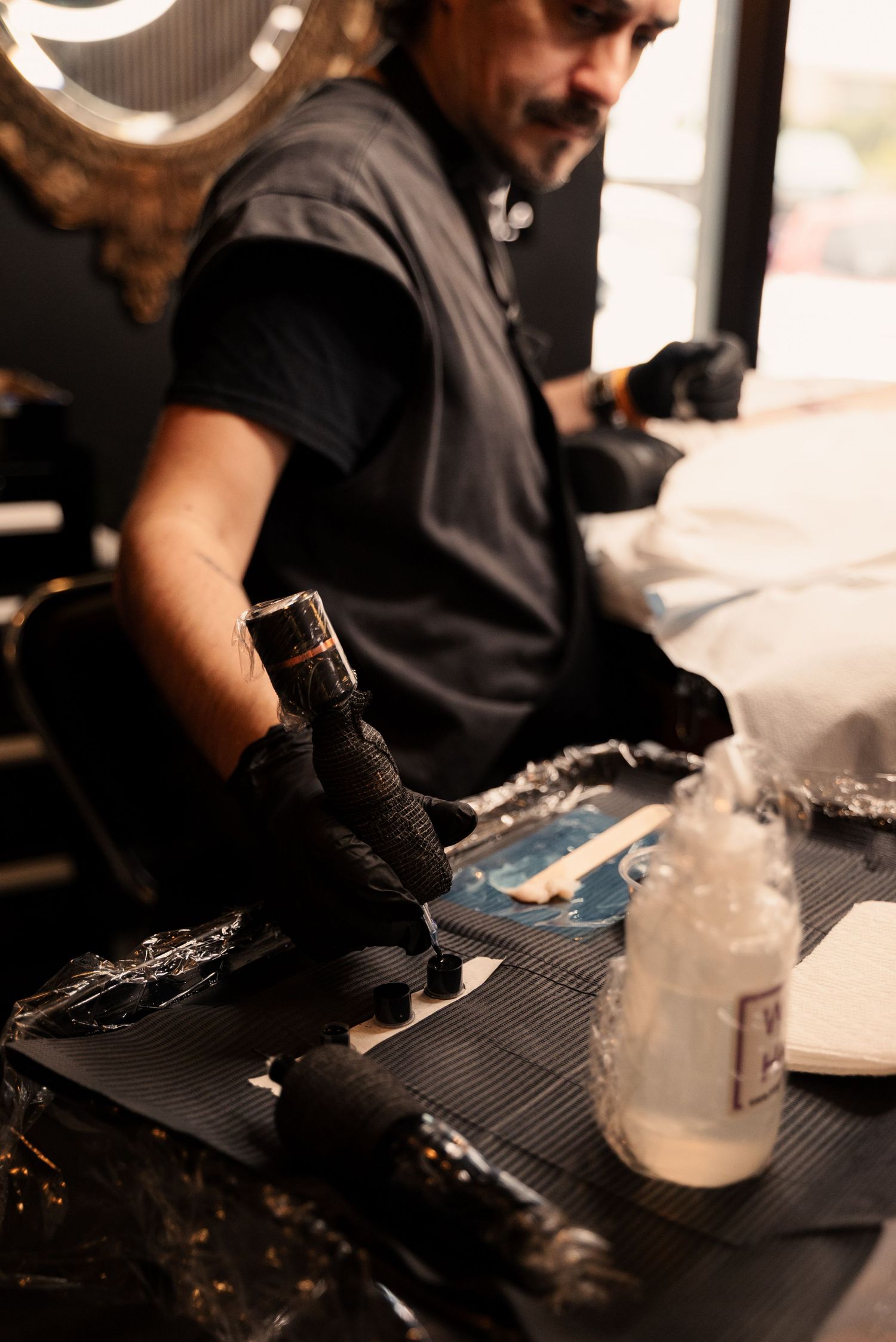 Tattoo artist preparing equipment and supplies on a black work surface.