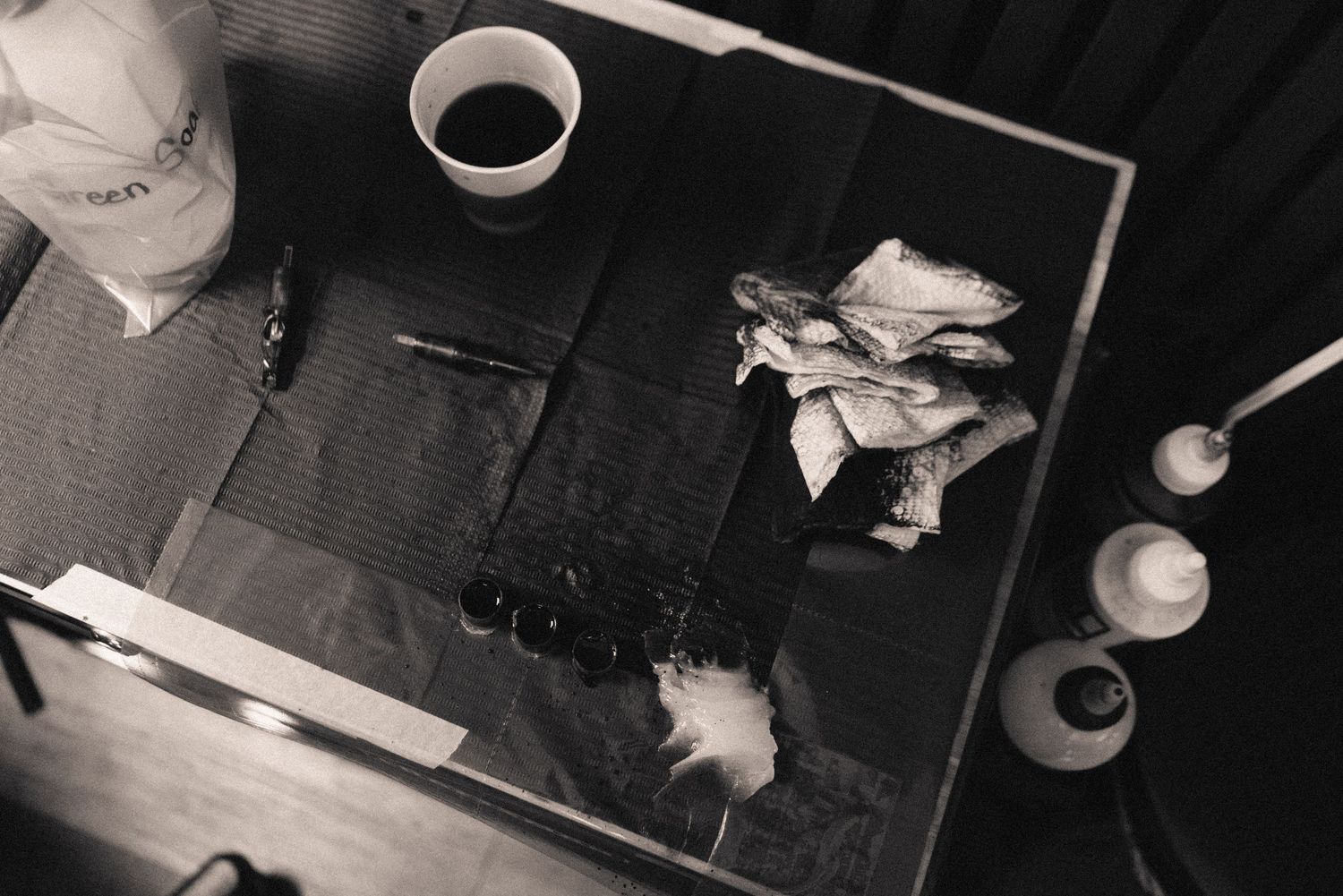 Overhead black and white view of a tattoo workspace with various tools and equipment.