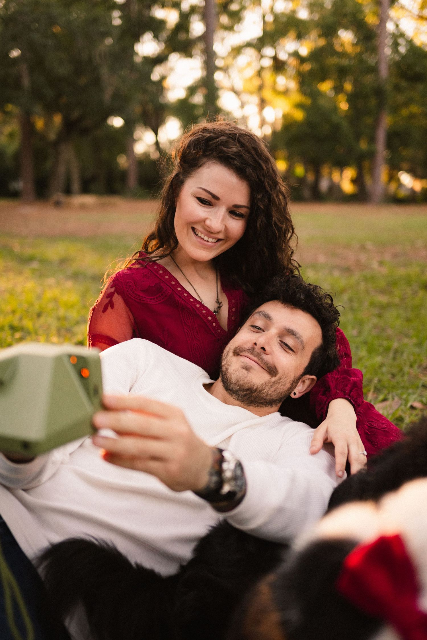 A couple relaxes together on grass during golden hour, sharing intimate moments.