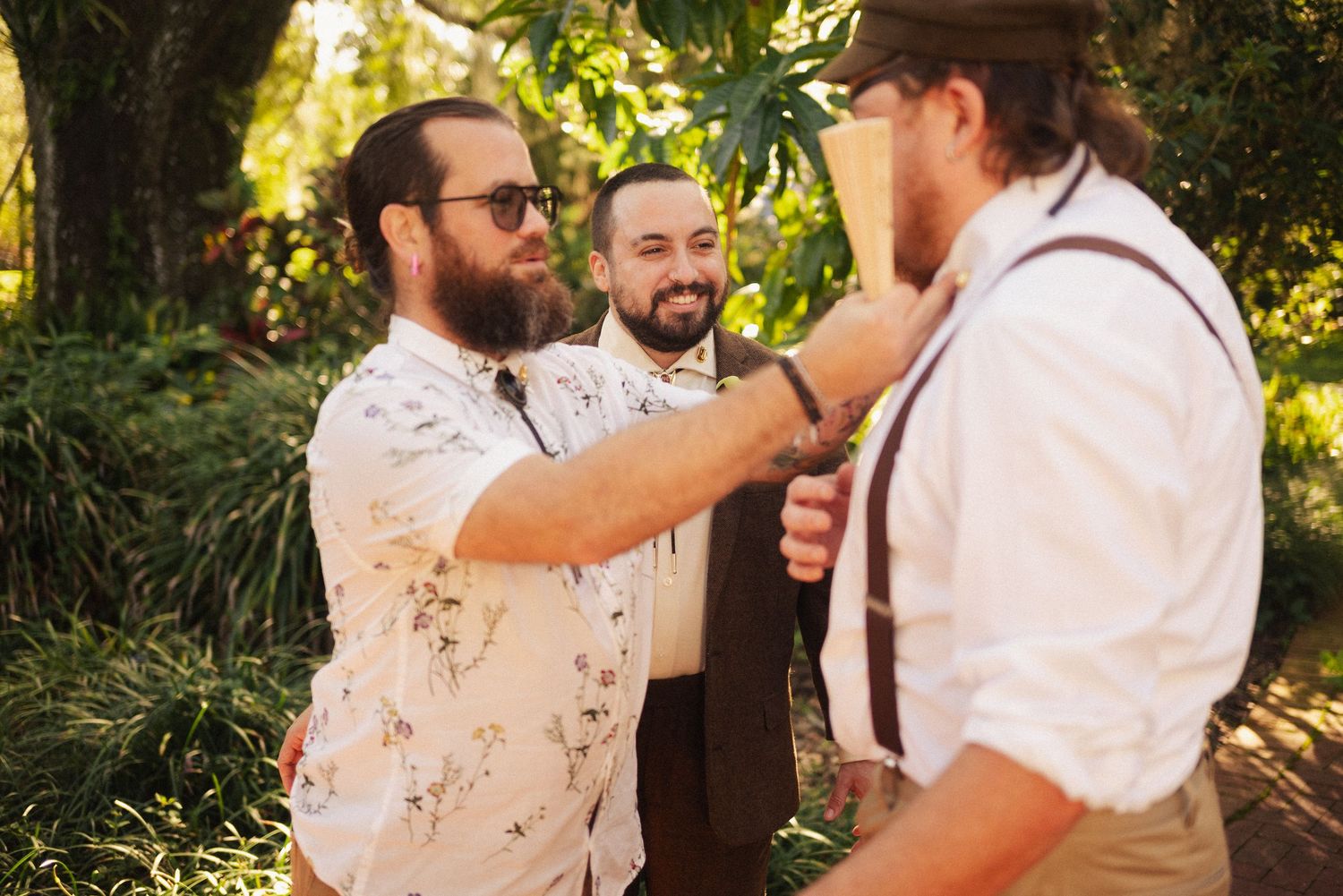 Wedding party members laugh together in an outdoor garden setting with natural lighting.