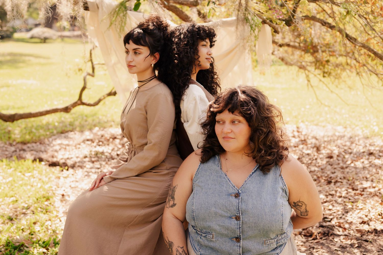 Three models pose together outdoors wearing casual vintage-inspired clothing in earth tones.