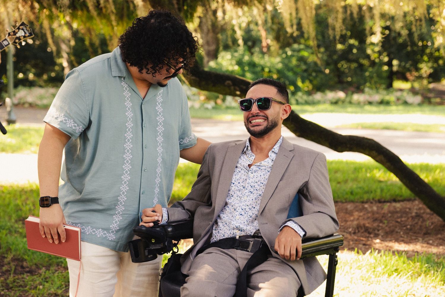 Wedding party relaxing outdoors in casual attire under trees.