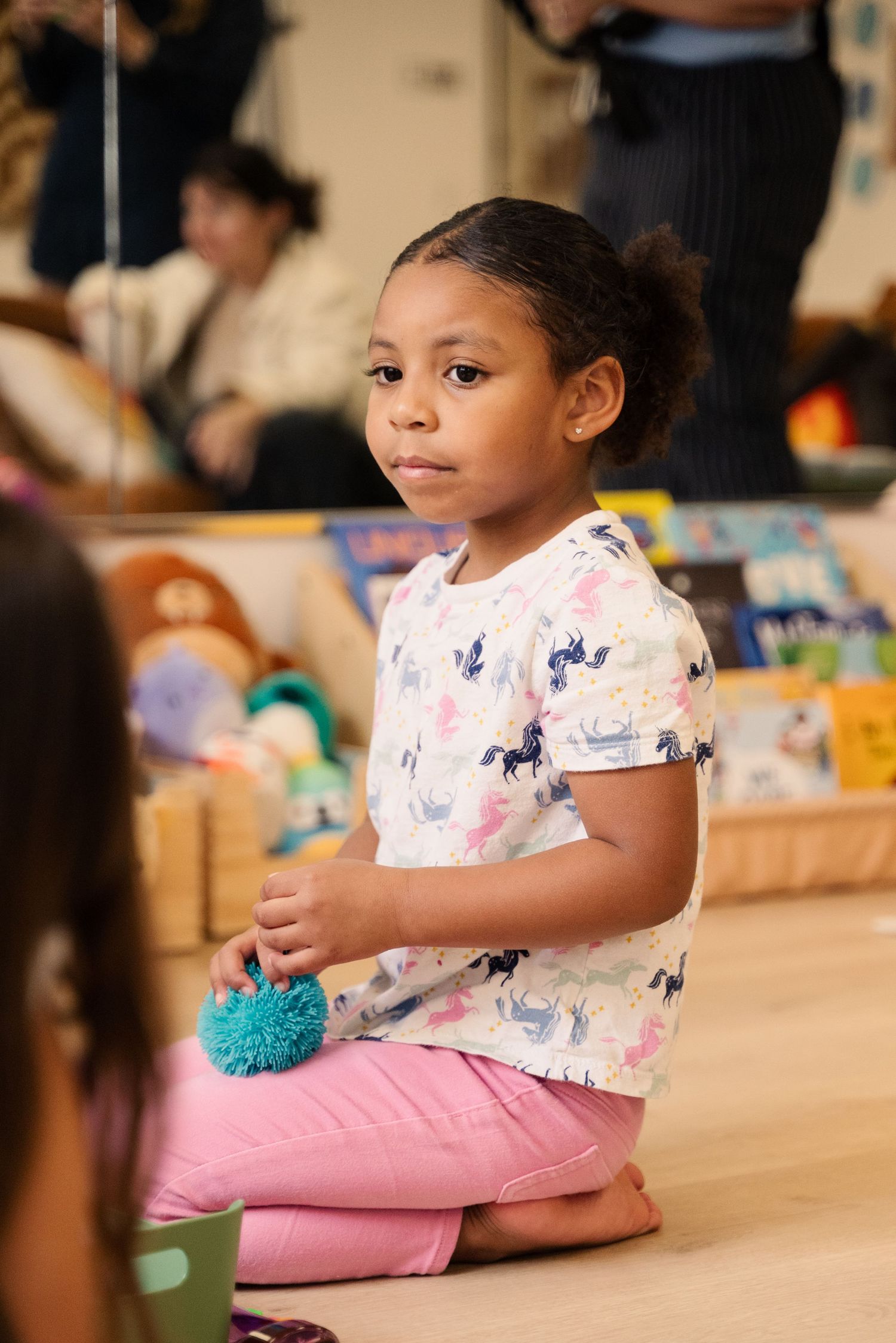 Young child in floral dress sitting on floor with colorful toys during playtime.