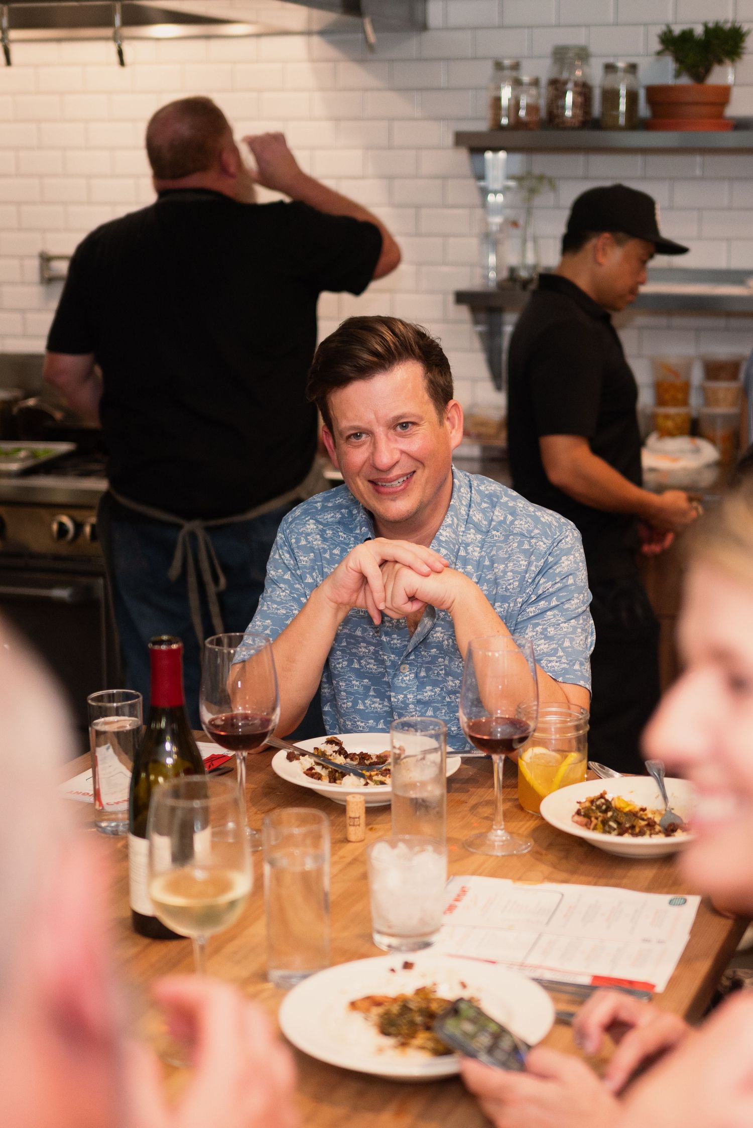 Restaurant patrons seated at wooden tables enjoying wine and conversation in a casual dining setting.