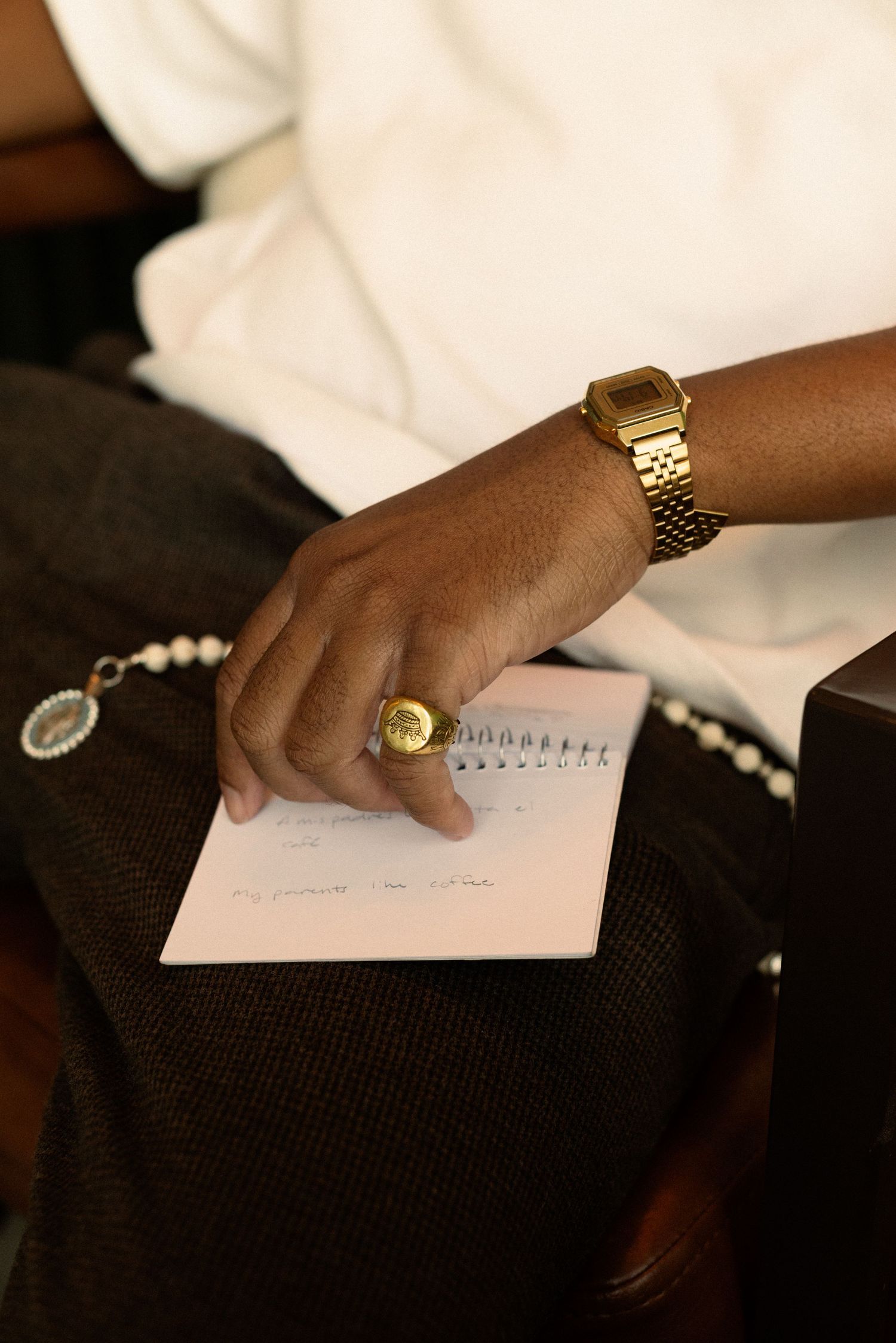 Close-up of hands with gold jewelry writing in a notebook on dark fabric.
