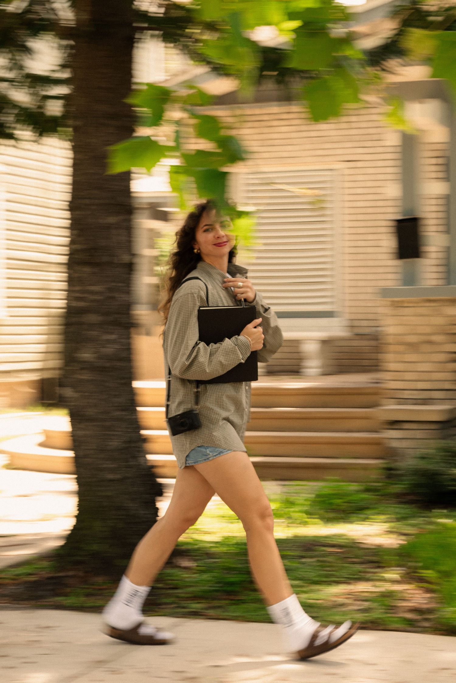 Motion blur shot of person running with notebook and camera through garden path.